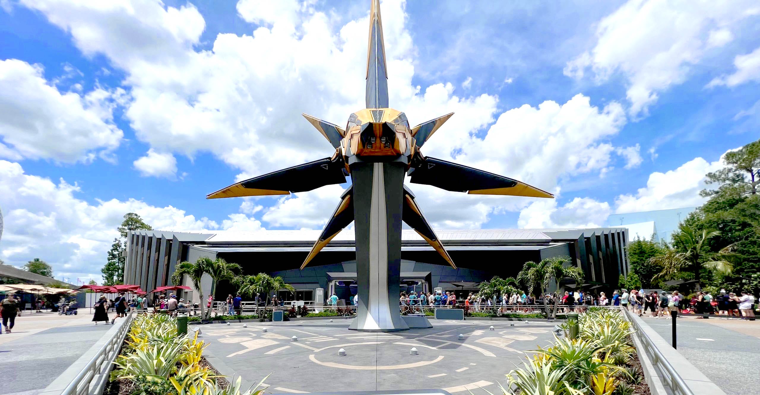 Top 10 EPCOT Rides - Guardians of the Galaxy cosmic rewind - A large spaceship statue stands in front of a modern building under a bright, partly cloudy sky, with people around.