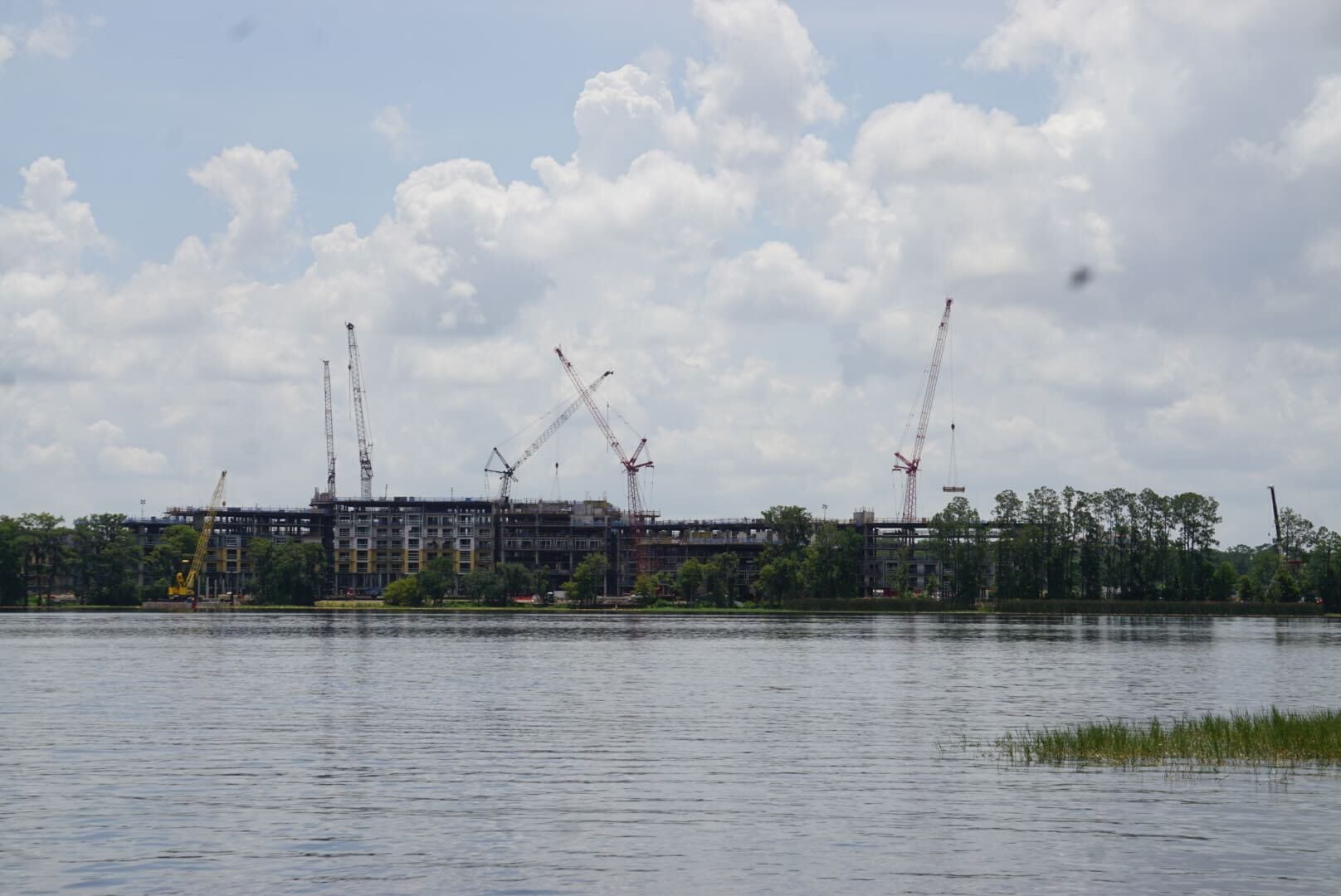 Cranes and a building under Lakeshore Construction are visible across a body of water with trees and clouds in the background.
