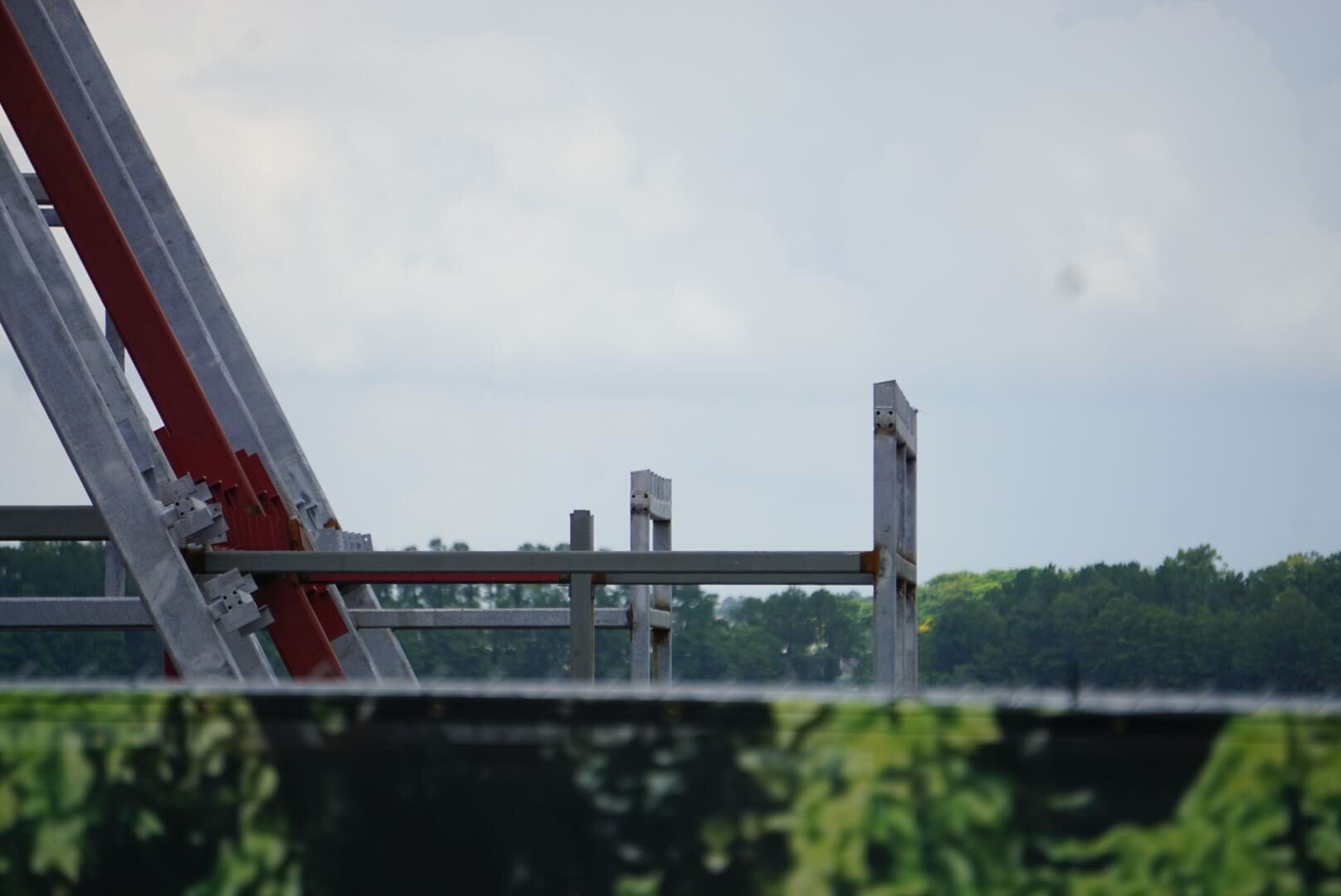Close-up of metal beams and structures by Lakeshore Construction, with green trees and a cloudy sky in the background.