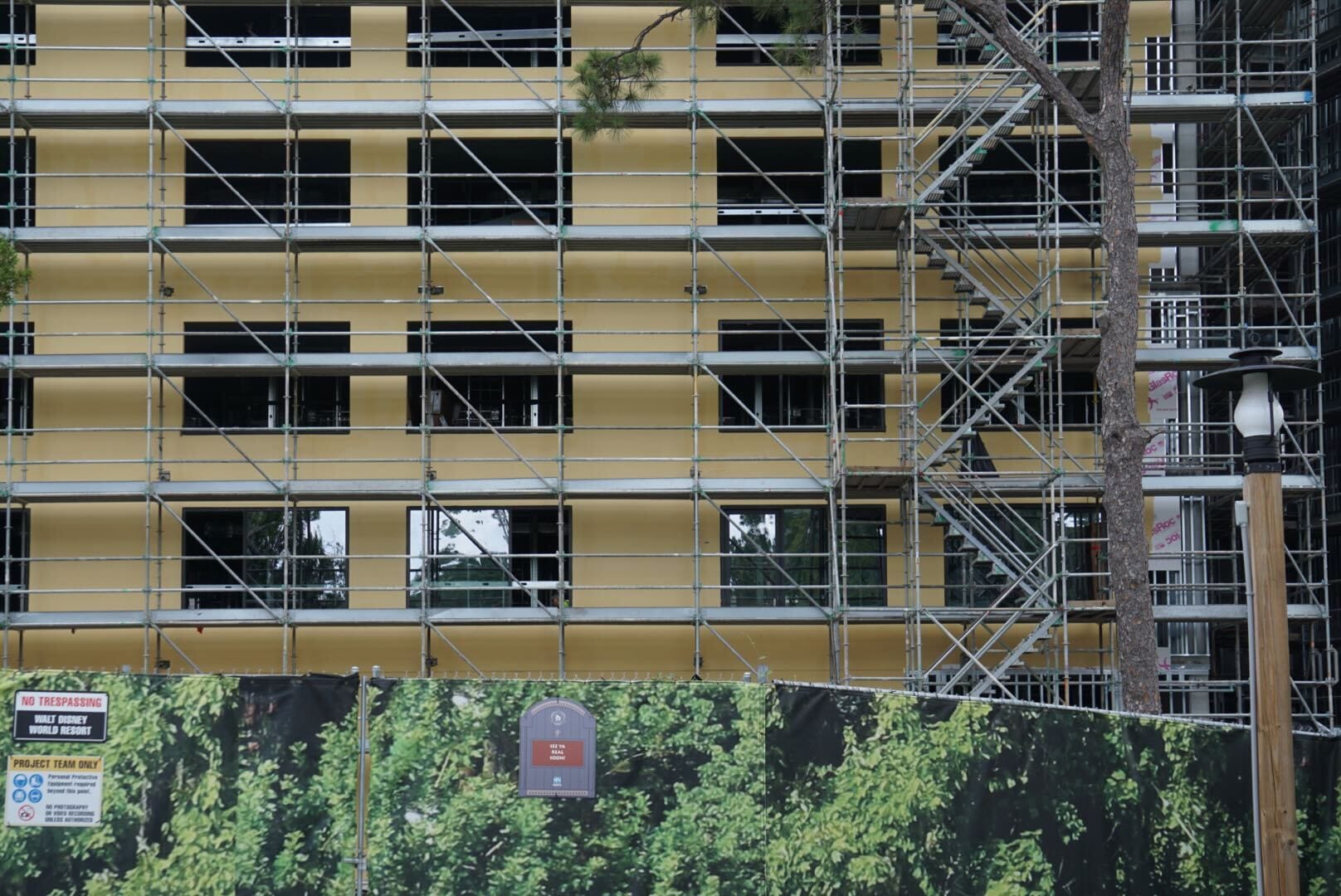 Lakeshore Lodge Construction: A building under construction with scaffolding, yellow insulation, and a green fence with tree graphics.