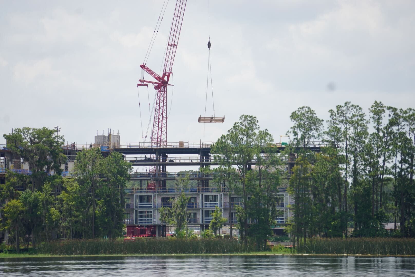 A crane lifts materials at a Lakeshore Construction site with trees and buildings in the background.