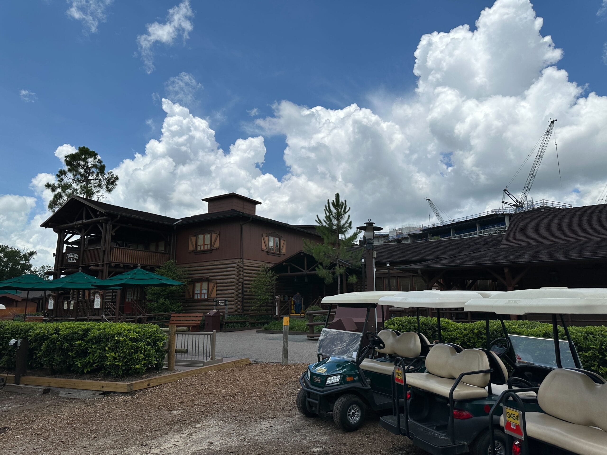 Lakeshore Lodge Construction: Wooden lodge under blue skies, golf carts in front, and cranes in the background.