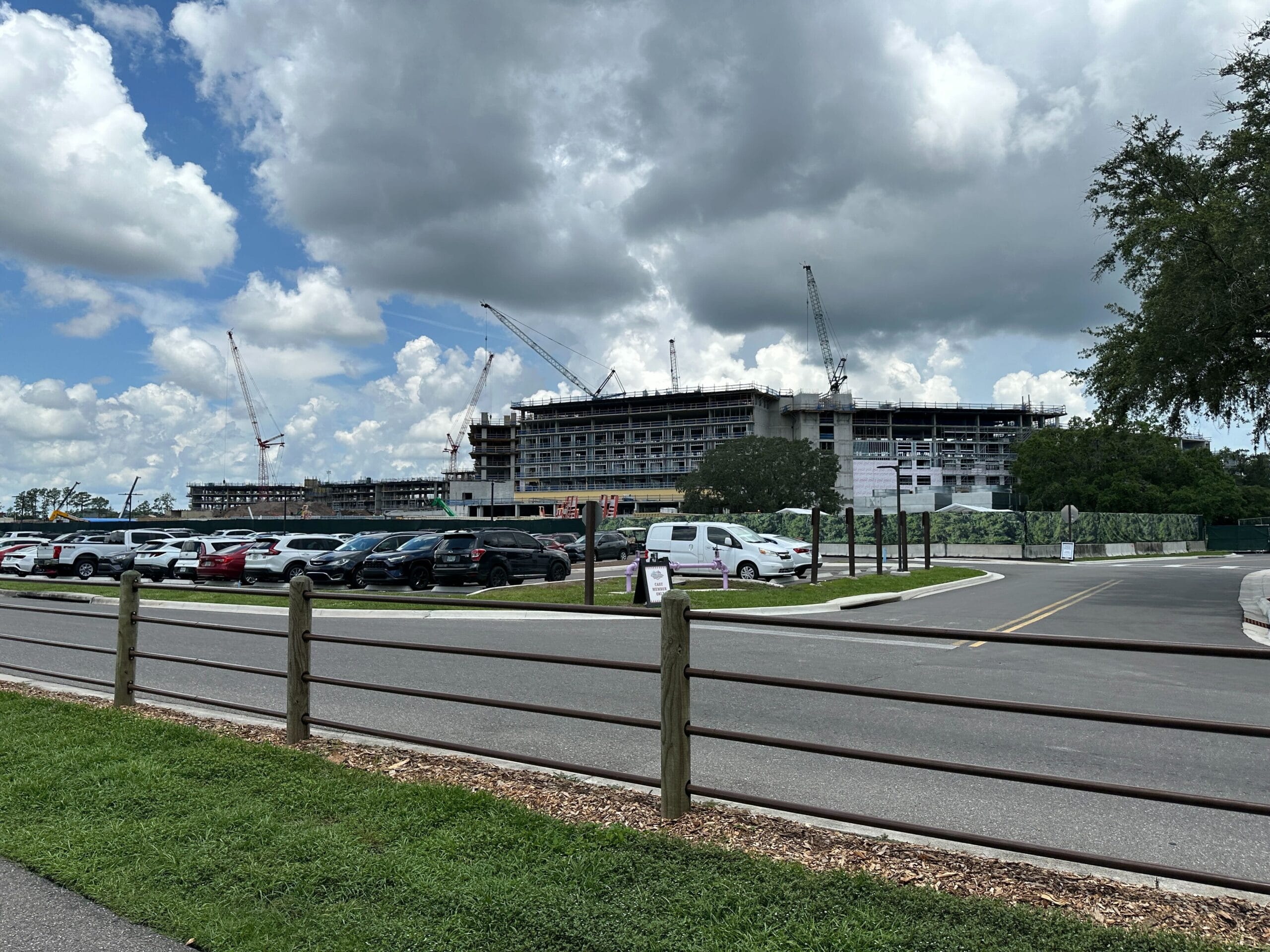 Lakeshore Lodge Construction: A large building rises with cranes behind a busy parking lot and a partly cloudy sky.