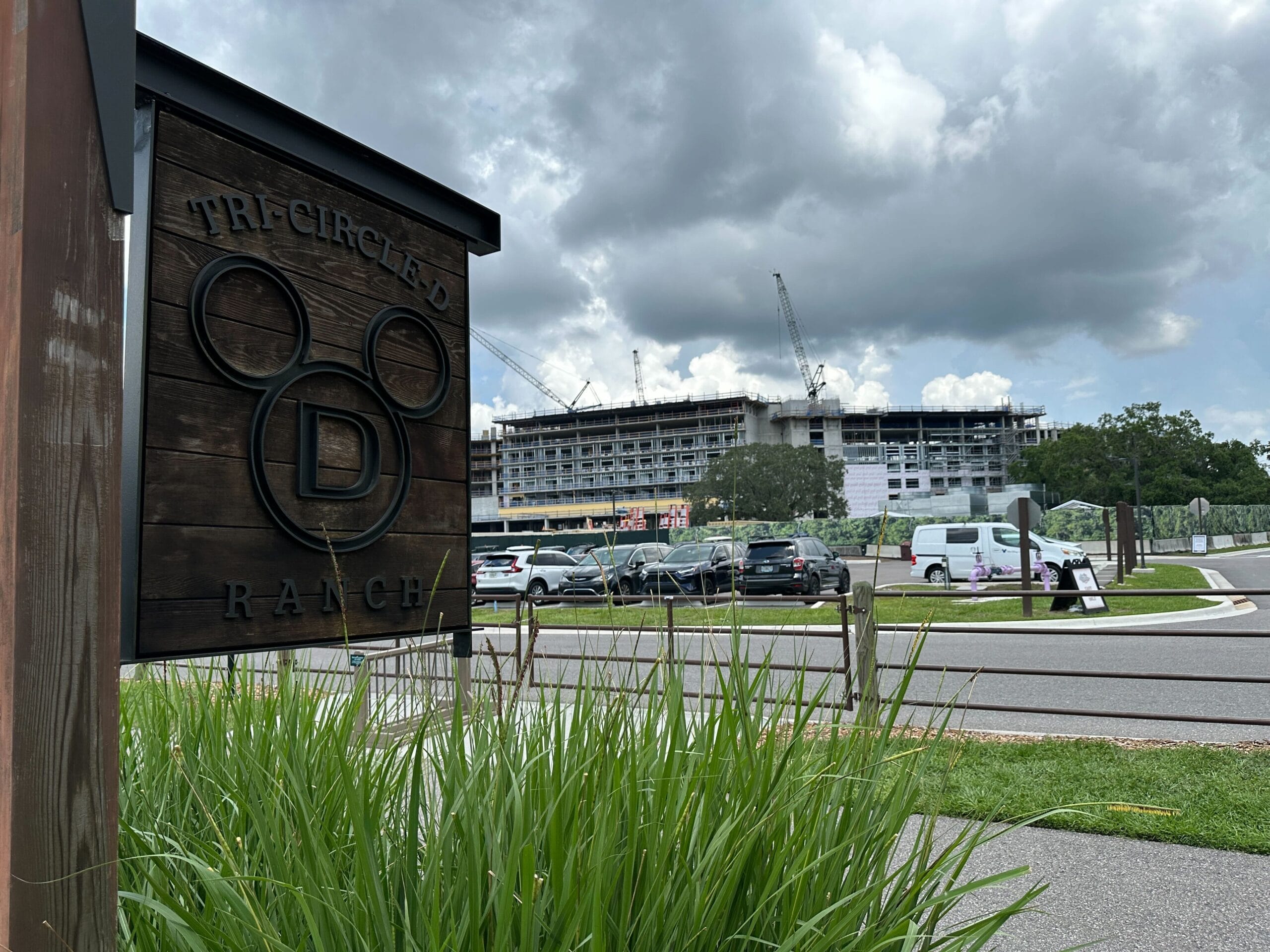 Sign for Tri-Circle-D Ranch with Lakeshore Lodge construction and parked cars visible in the background.