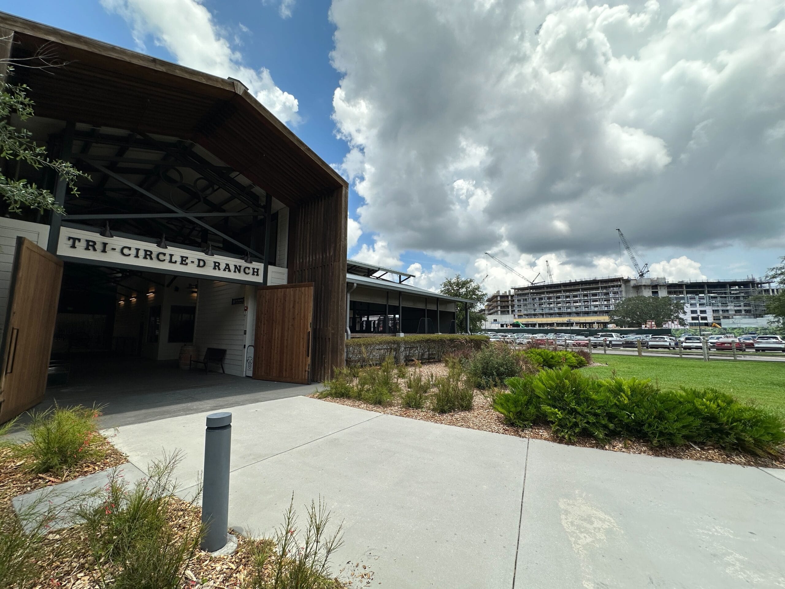 Open wooden barn labeled "Tri-Circle-D Ranch" beside Lakeshore Lodge construction, under a cloudy sky.