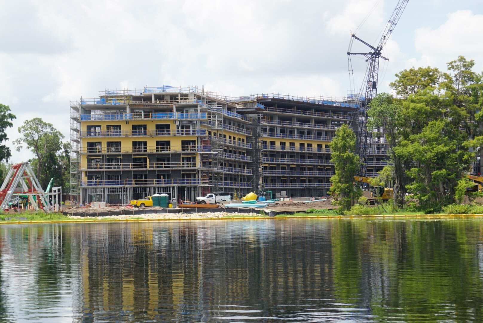 Lakeshore Lodge under construction by a lake, with scaffolding, cranes, and materials onsite.