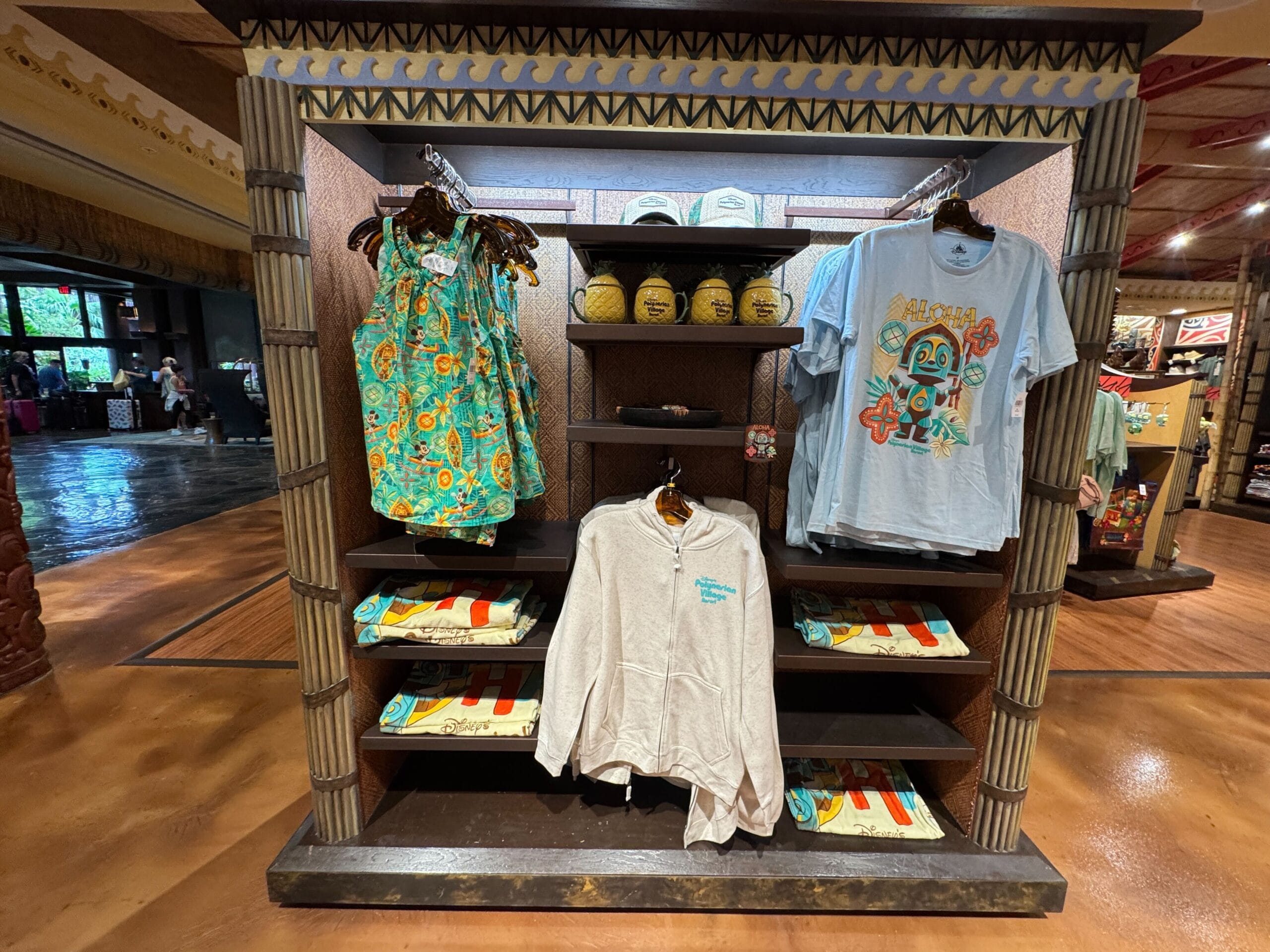 Display of tropical-themed shirts, dresses, towels, and basketballs in a store with decorative columns and brown floor.
