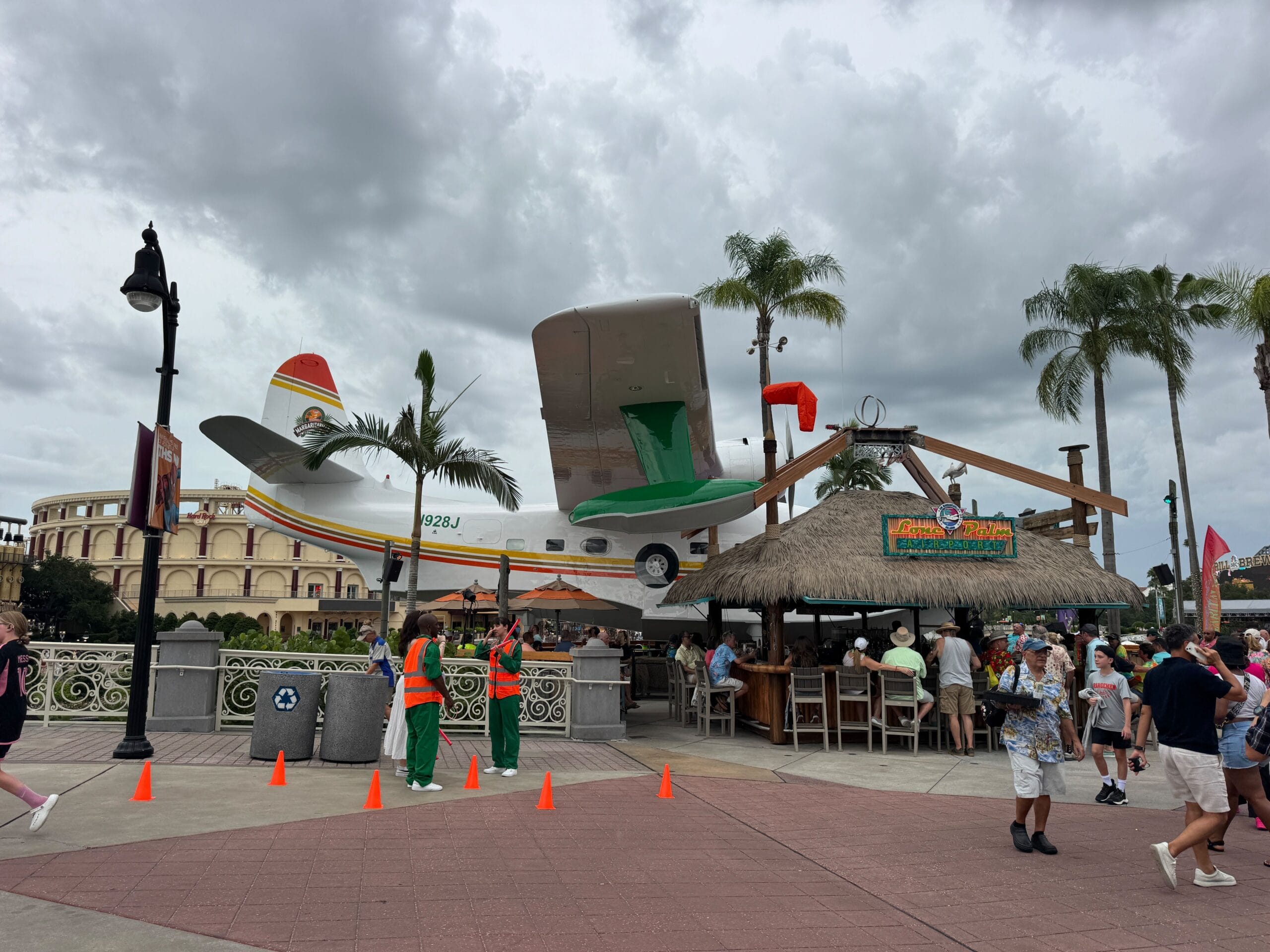 A seaplane, the Hemisphere Dancer, is displayed behind a Margaritaville bar with people mingling under cloudy skies.