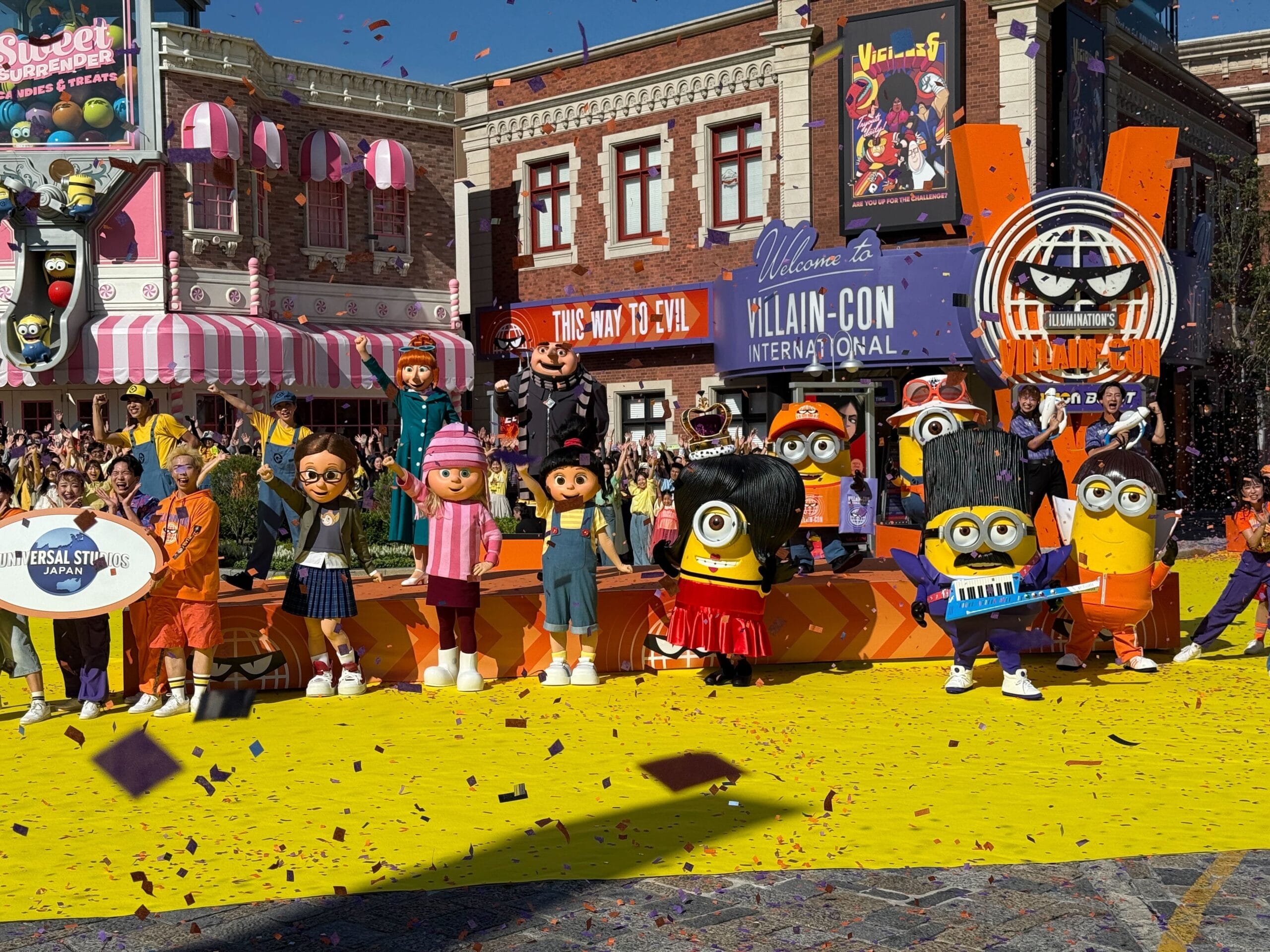 Minions and other characters pose on a yellow stage at Universal Studios Japan’s lively Grand Opening Ceremony with confetti falling.