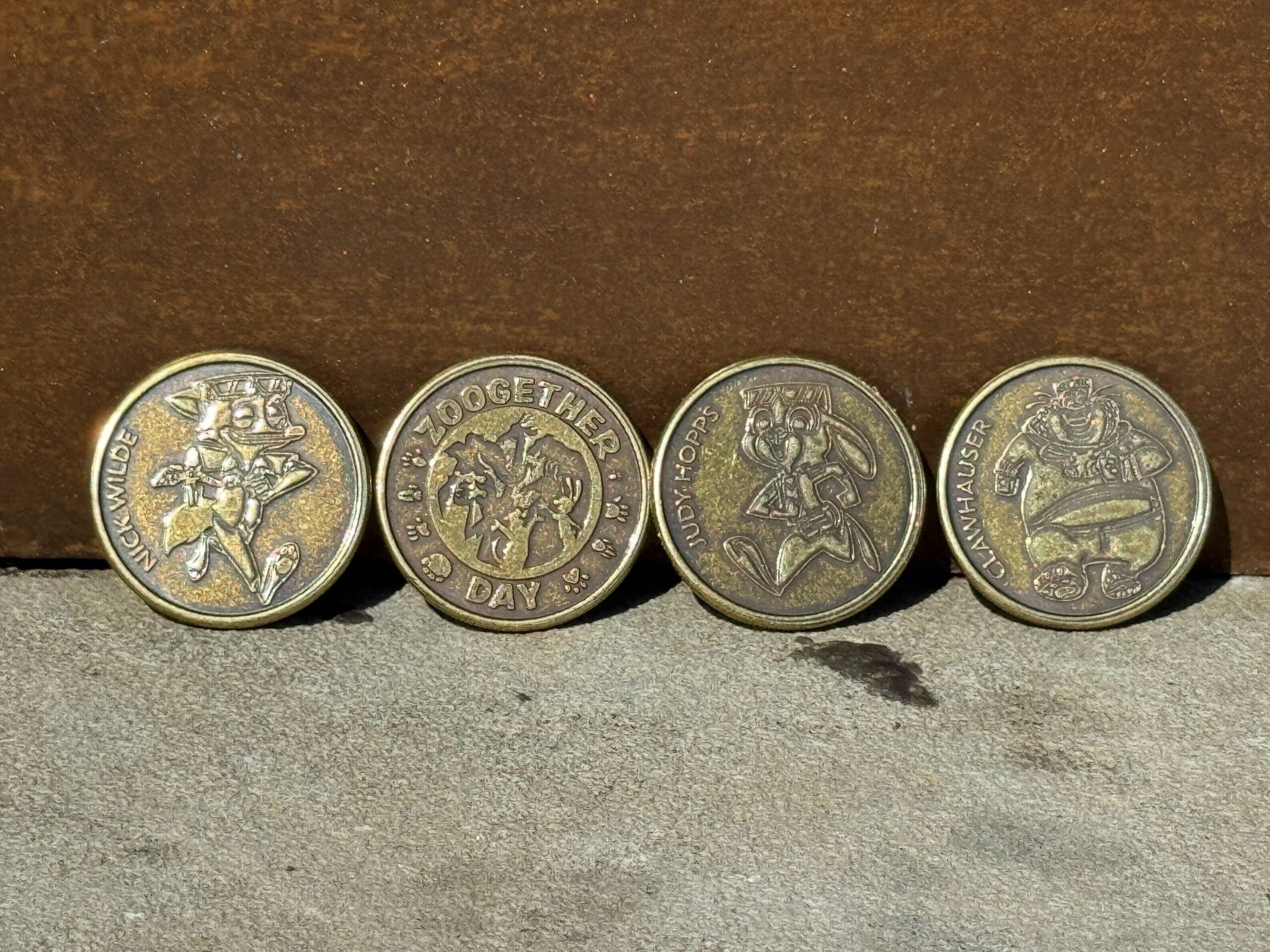 Four gold-colored collectible medallions featuring Zootopia animal characters, arranged in a neat row on a flat surface.