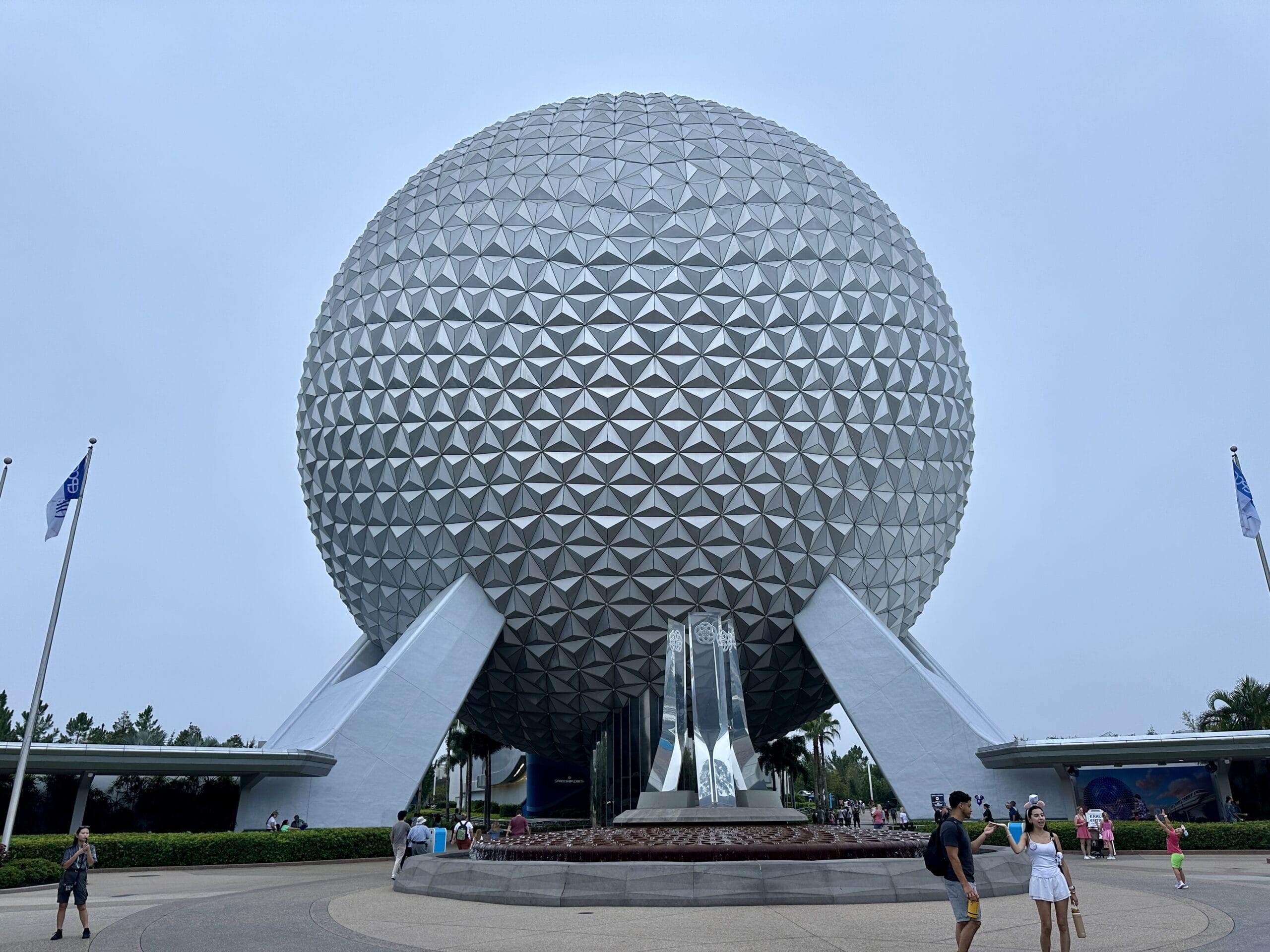 A large geodesic sphere at EPCOT in Walt Disney World, with people strolling by on a cloudy day.