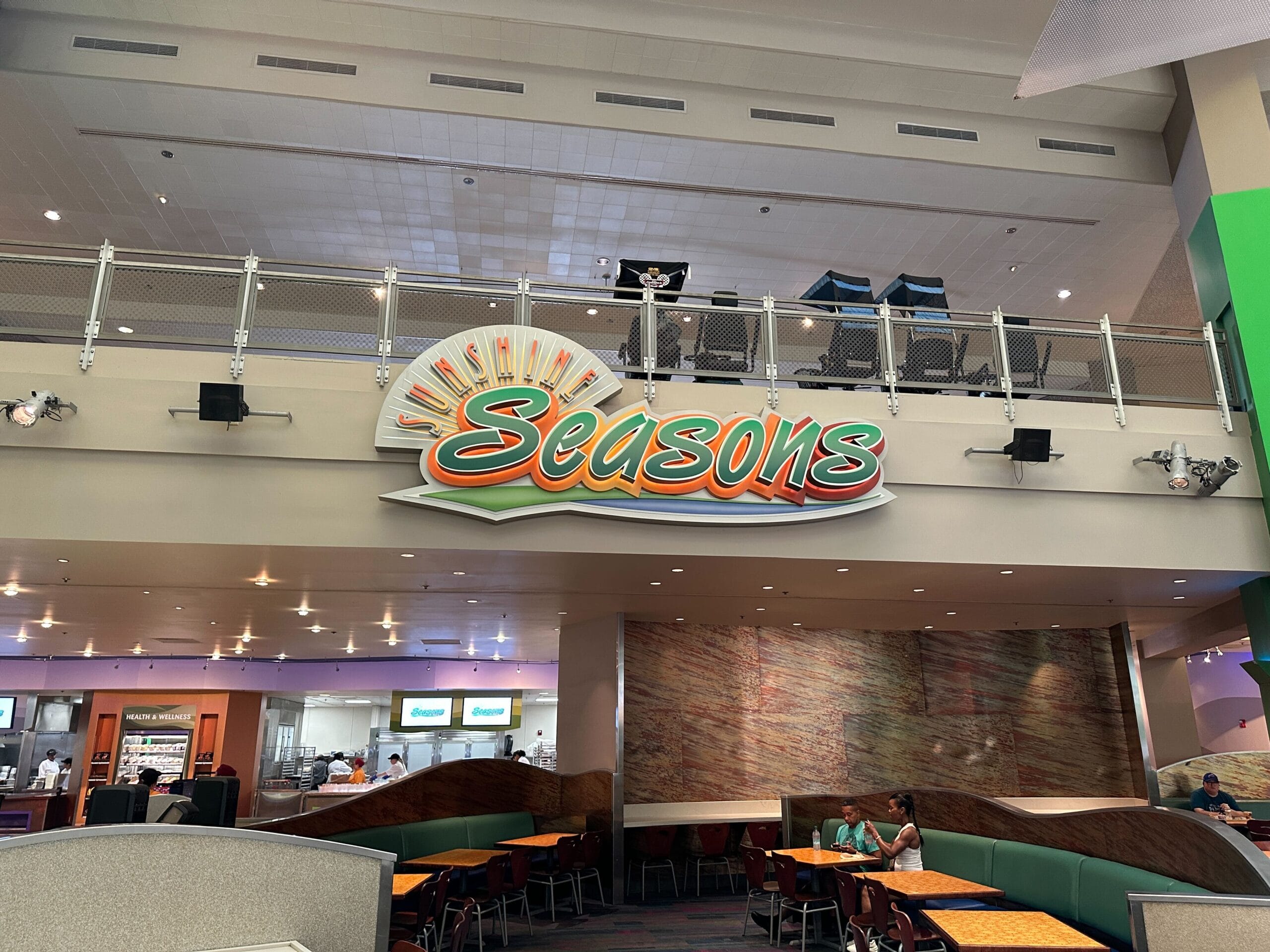 Seasons restaurant sign with stylized sun above a dining area and people seated at tables below.