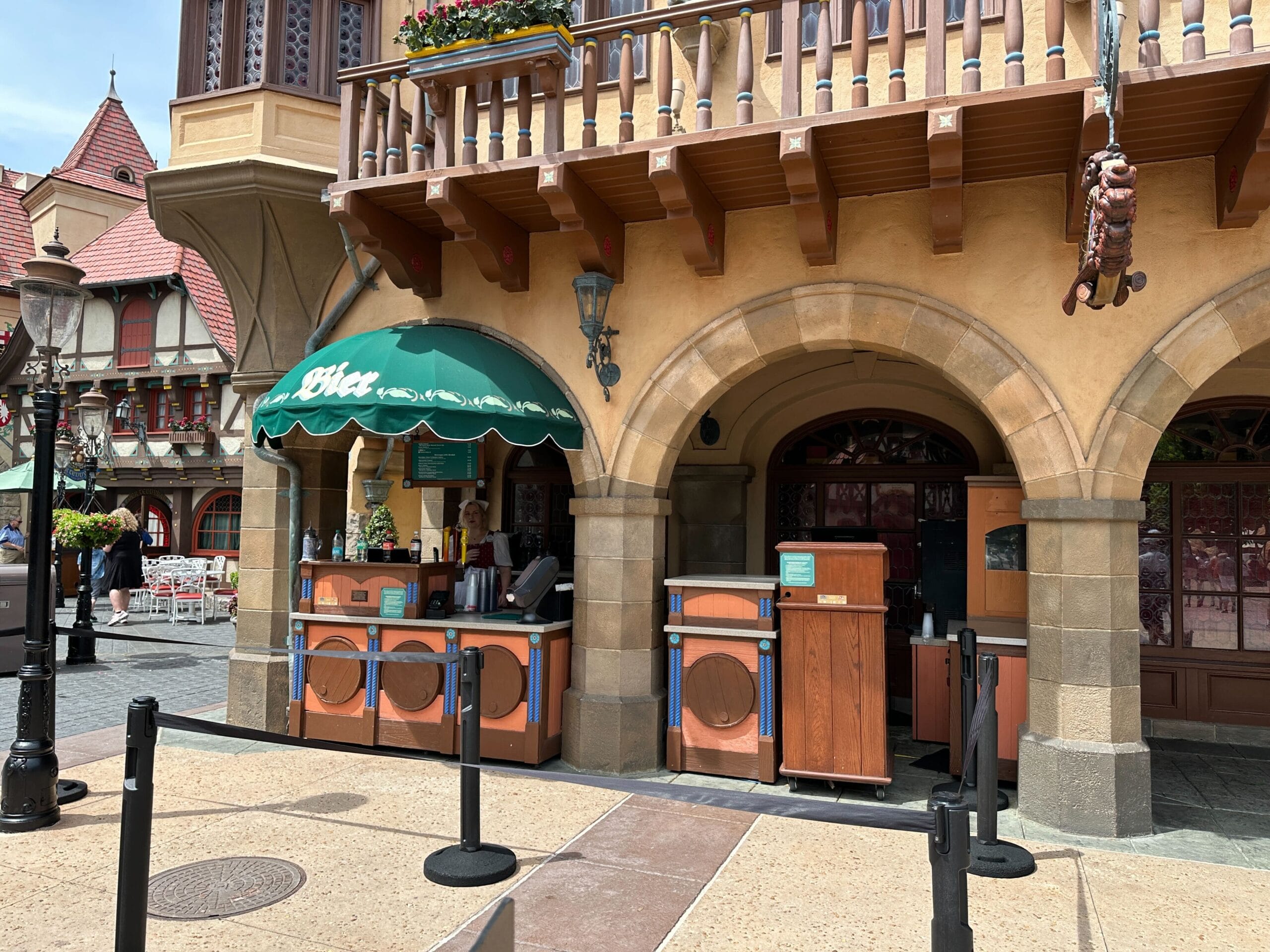 Outdoor food stand with a green awning and faux washing machines under a stone archway in a themed village setting.