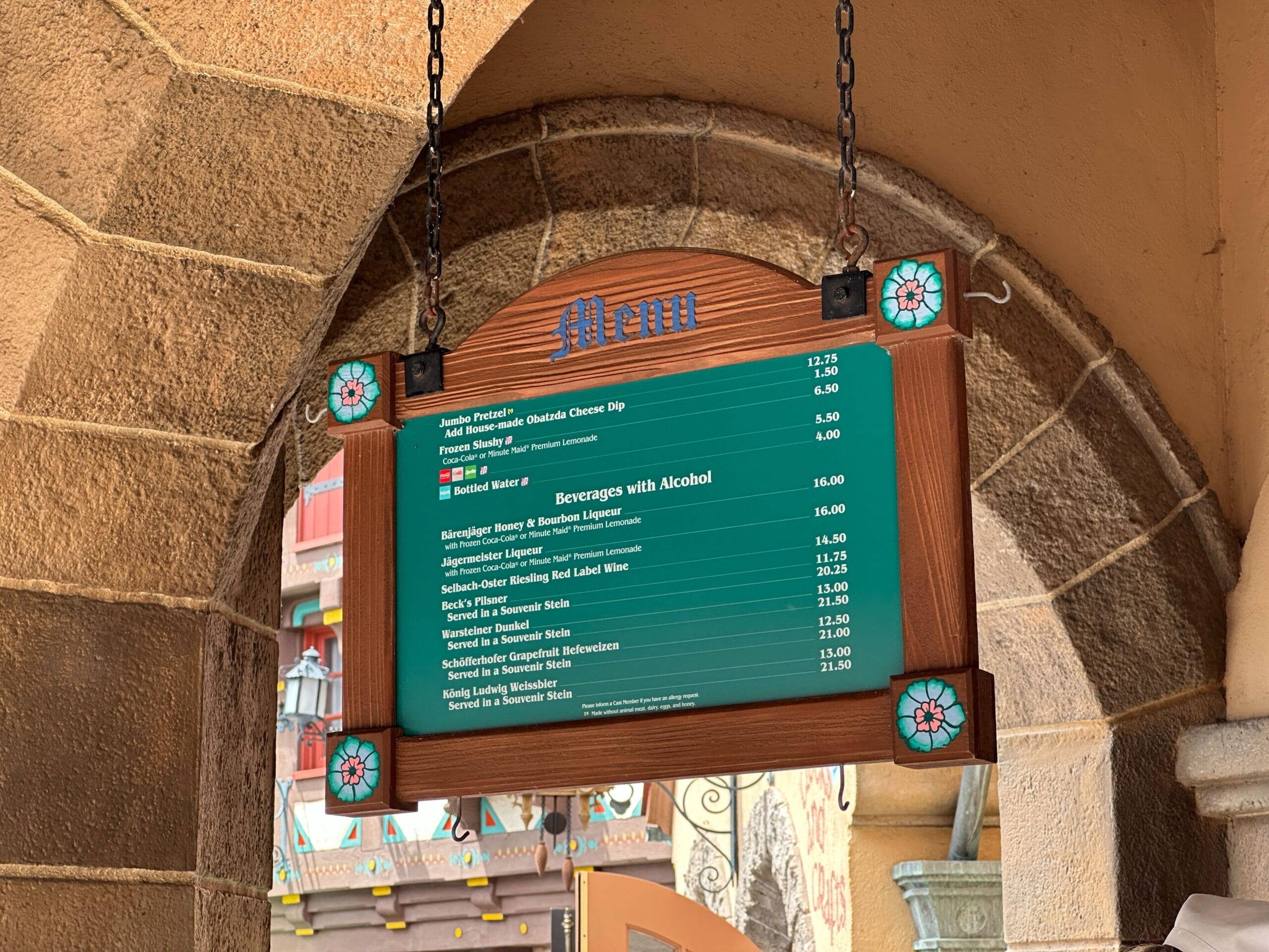 A hanging restaurant menu board with food and beverage options, set in a stone archway with colorful tile accents.