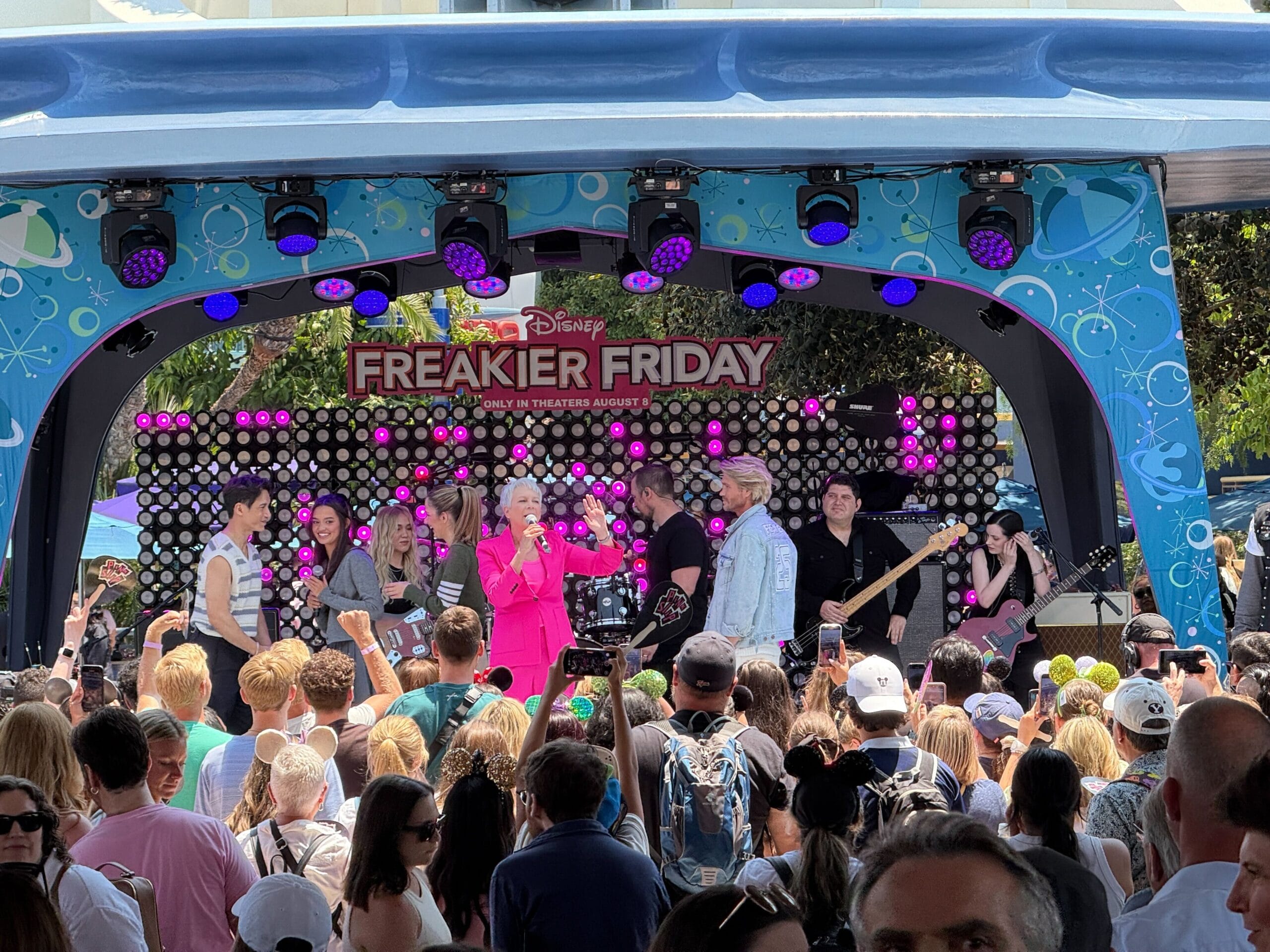A crowd watches a live band perform on an outdoor Disney stage decorated for "Freaky Friday.