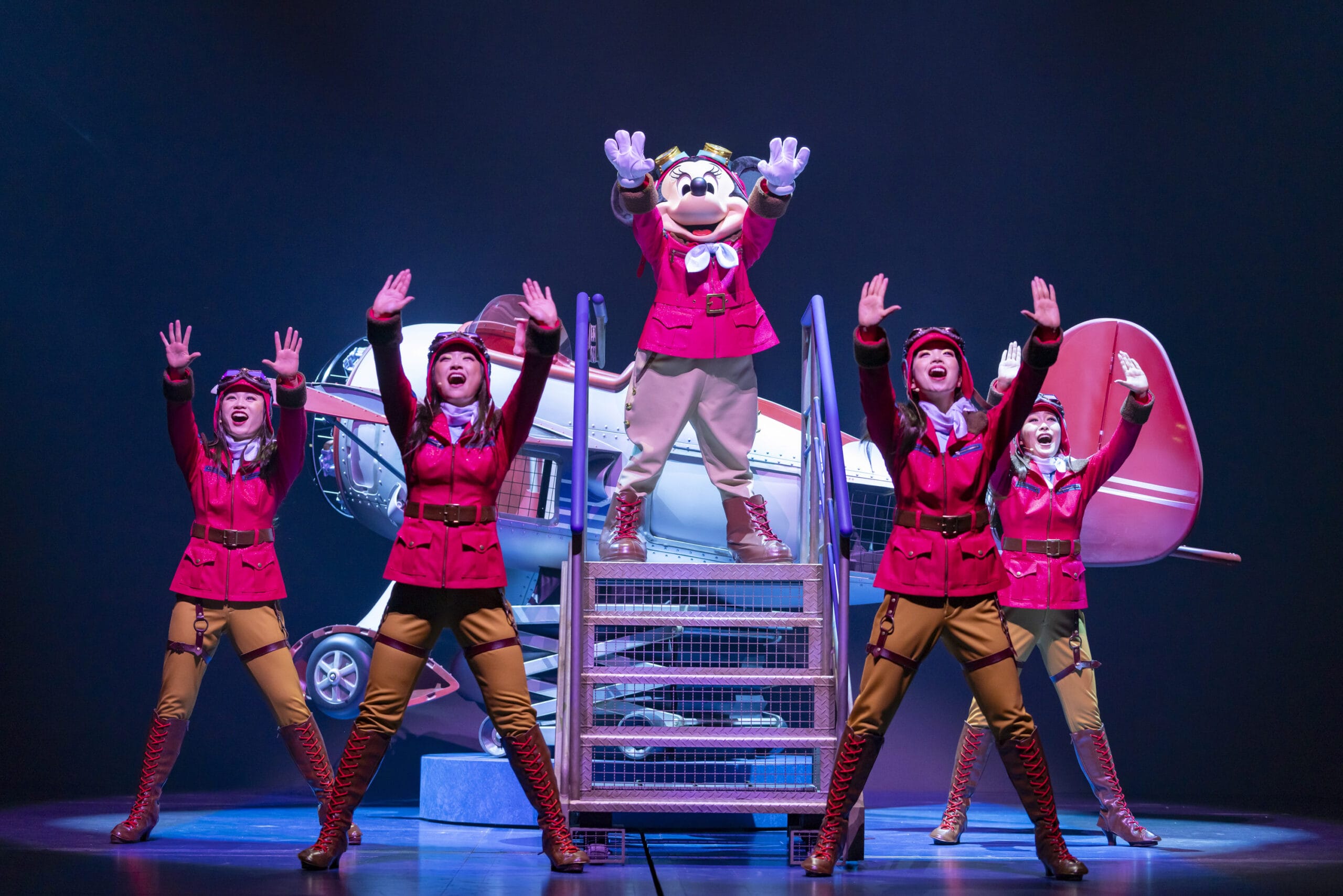 Five performers in aviator costumes pose by a prop plane at Tokyo DisneySea, where dreams take flight on stage.