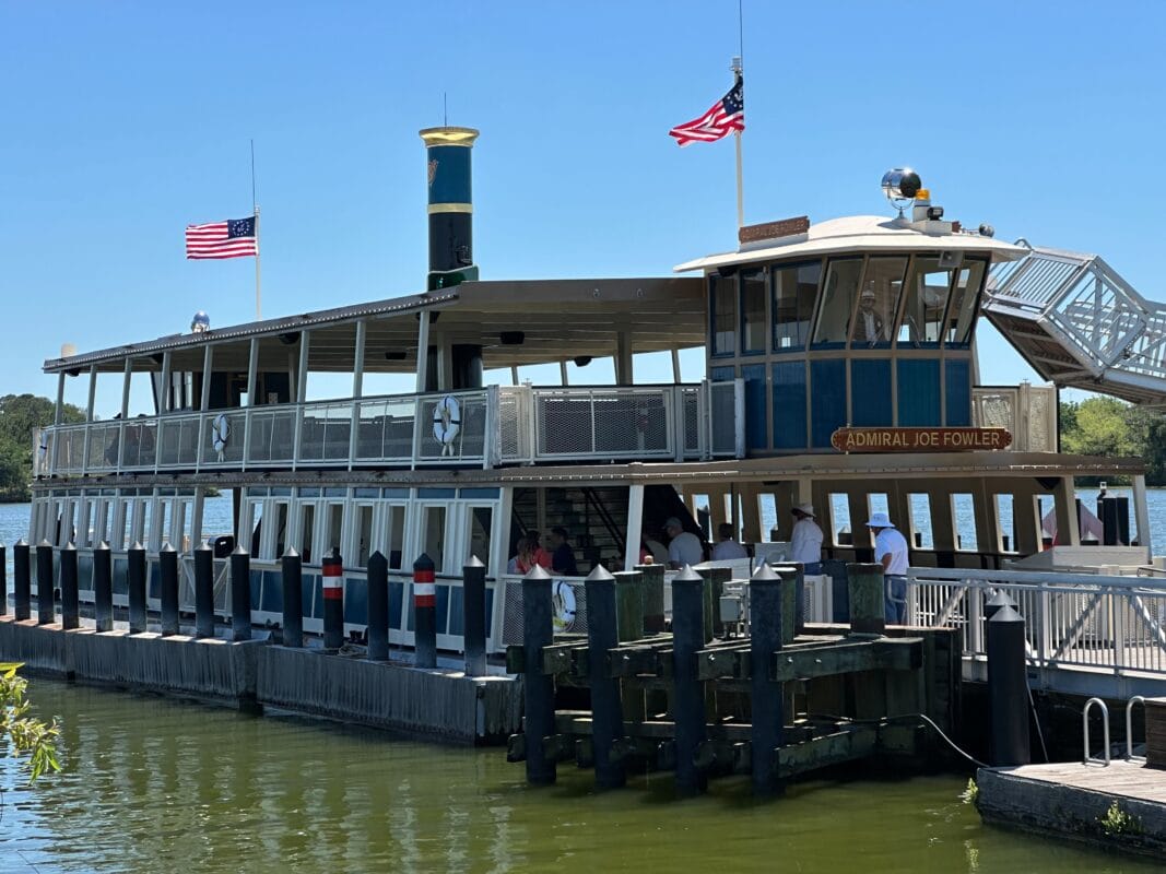 A ferry boat named Admiral Joe Fowler docked at the Disney Transportation and Ticket Center pier, with people boarding and American flags flying.