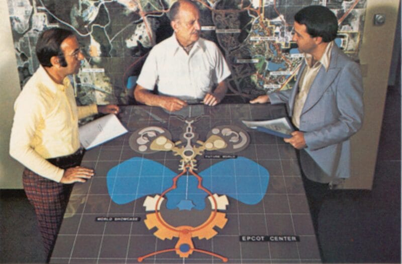 Three men discuss a large EPCOT Center model, exploring Walt Disney World history with maps displayed on the wall behind them.