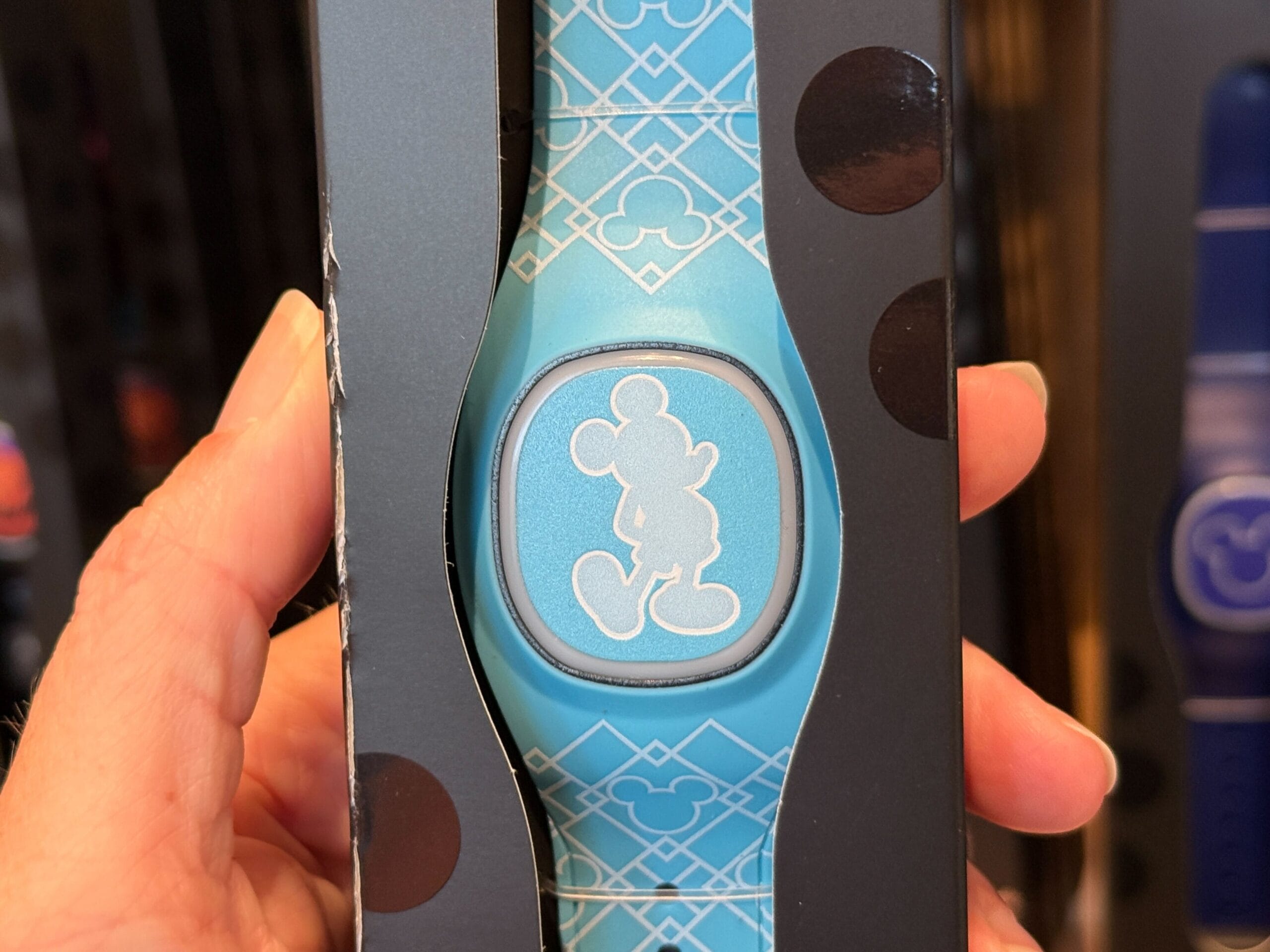 Hand holding a blue Disney MagicBand with a silver Mickey Mouse silhouette in the center.