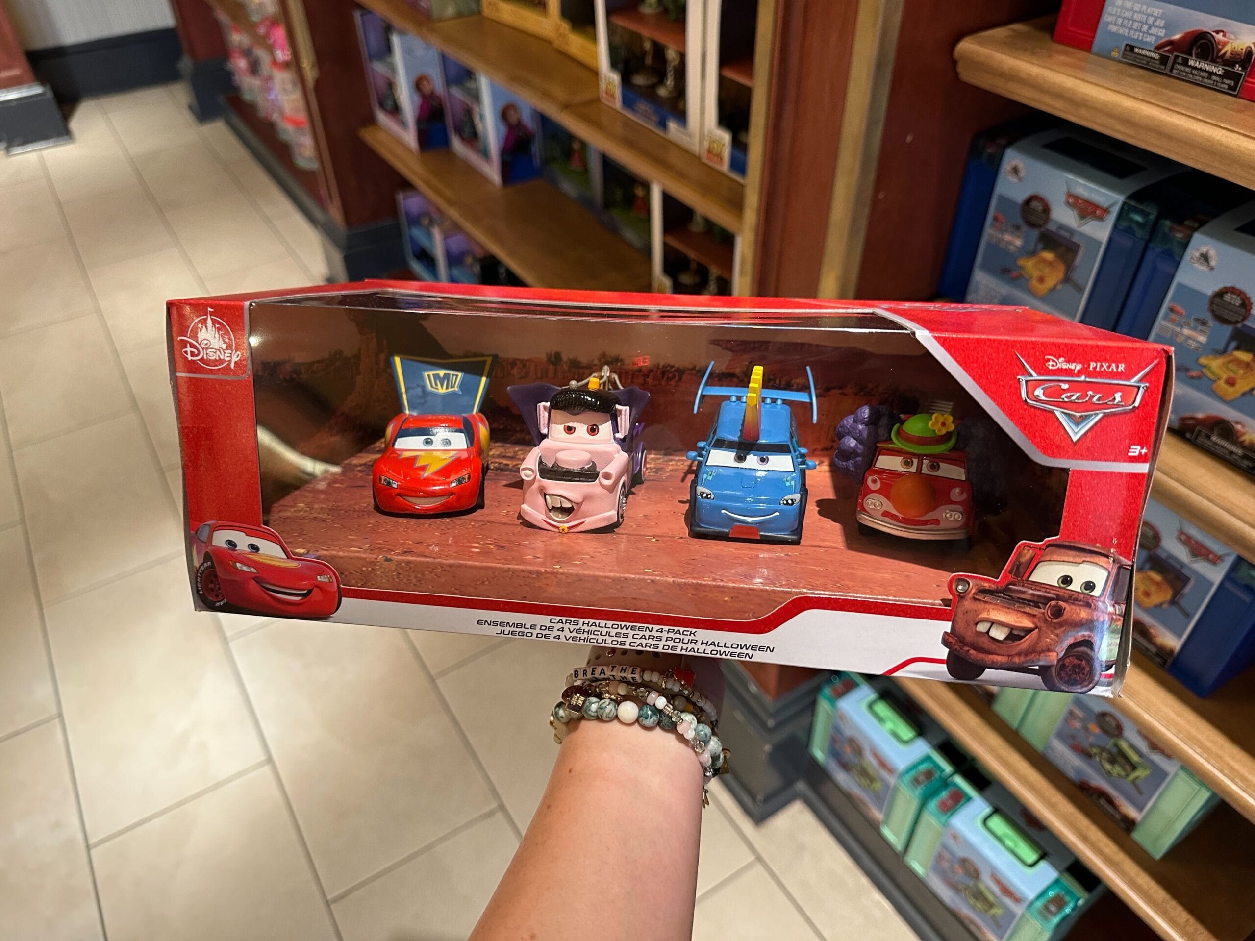 A hand holds a box with four Disney Pixar Cars toy cars on a store shelf.