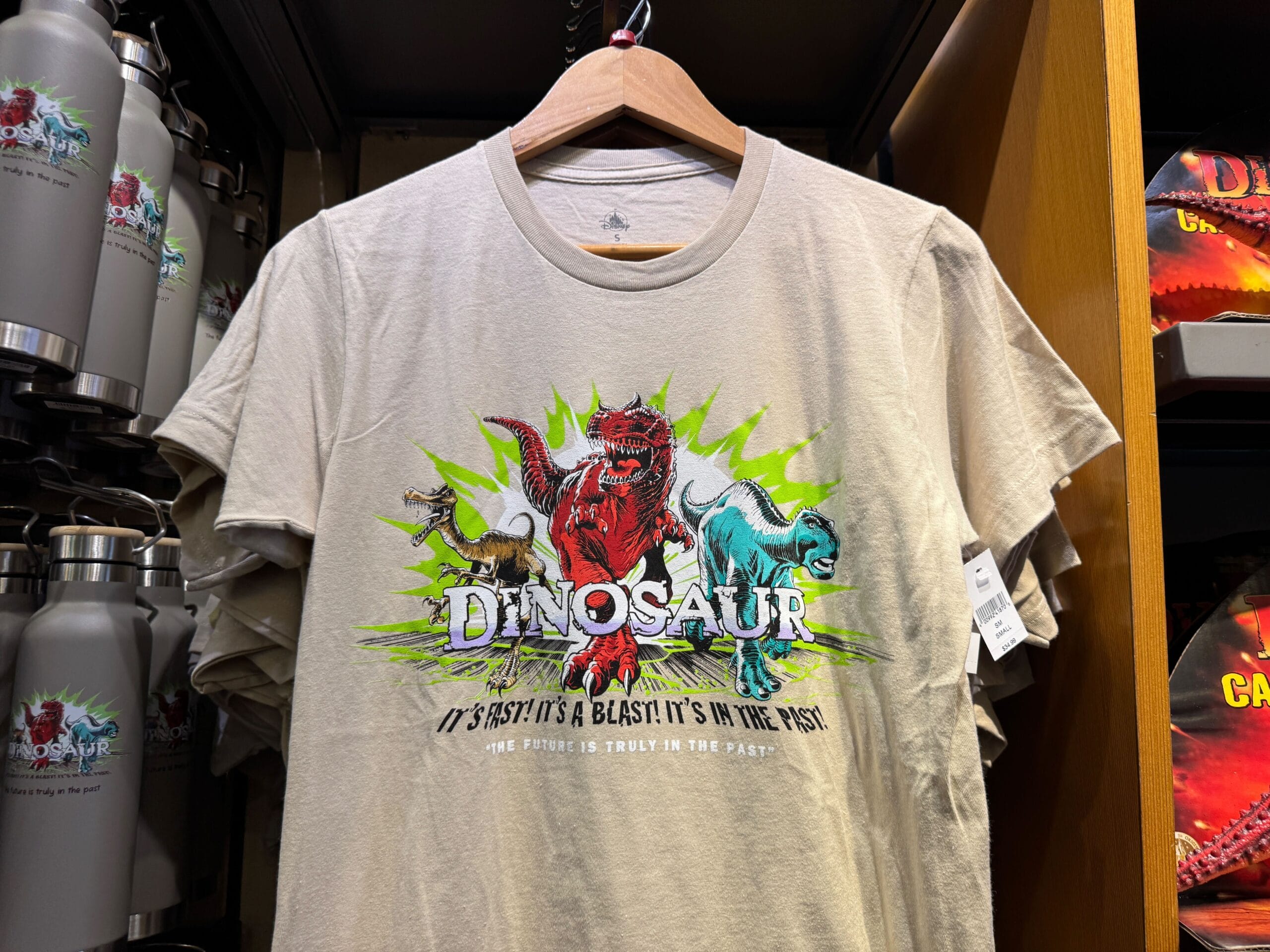 Beige t-shirt with colorful dinosaurs and text: "Dinosaur. It's fast. It's a blast. It's in the past.