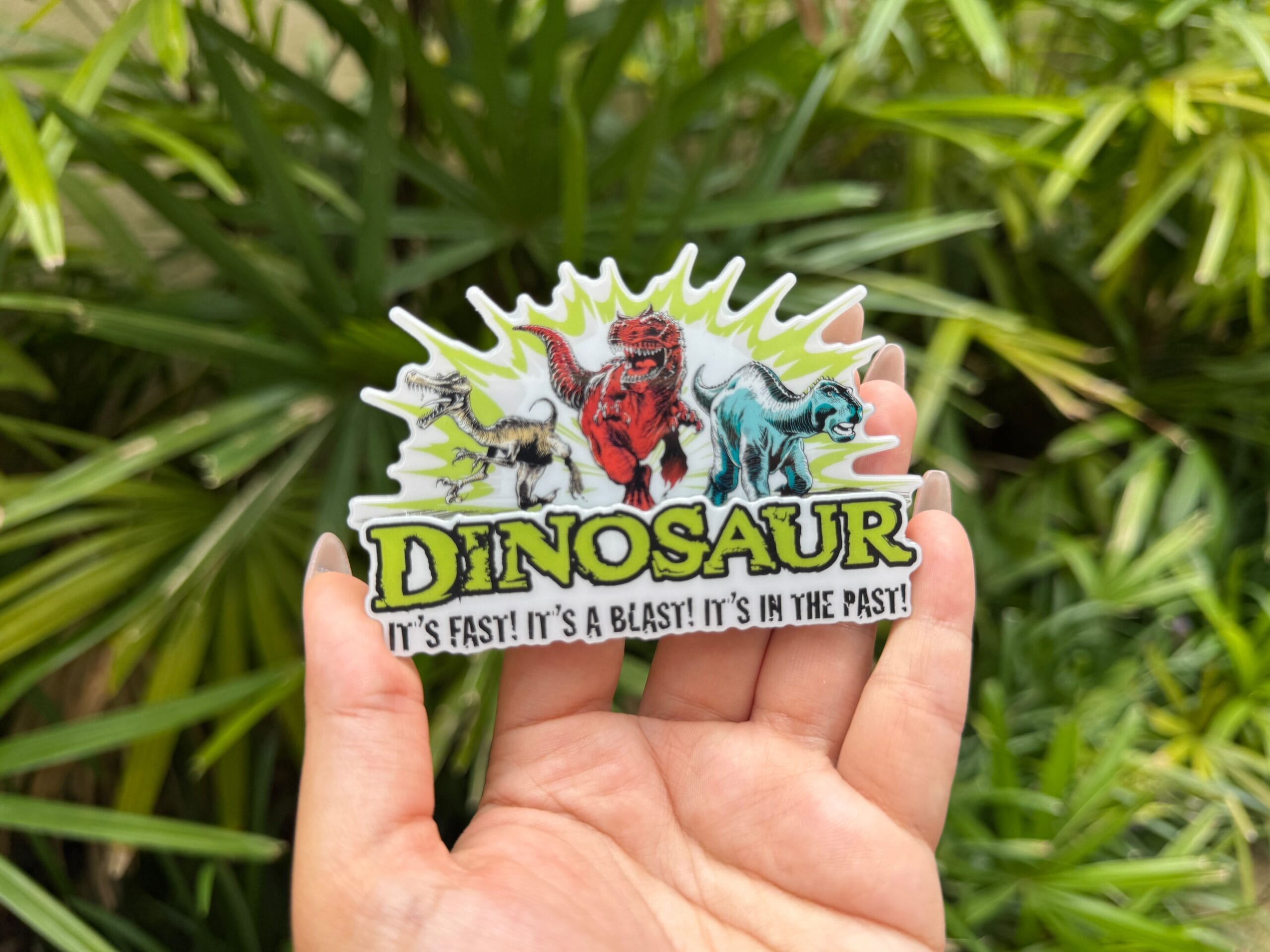 A hand holds a “DINOSAUR” sticker with cartoon dinosaurs and the slogan "It’s fast! It’s a blast! It’s in the past!