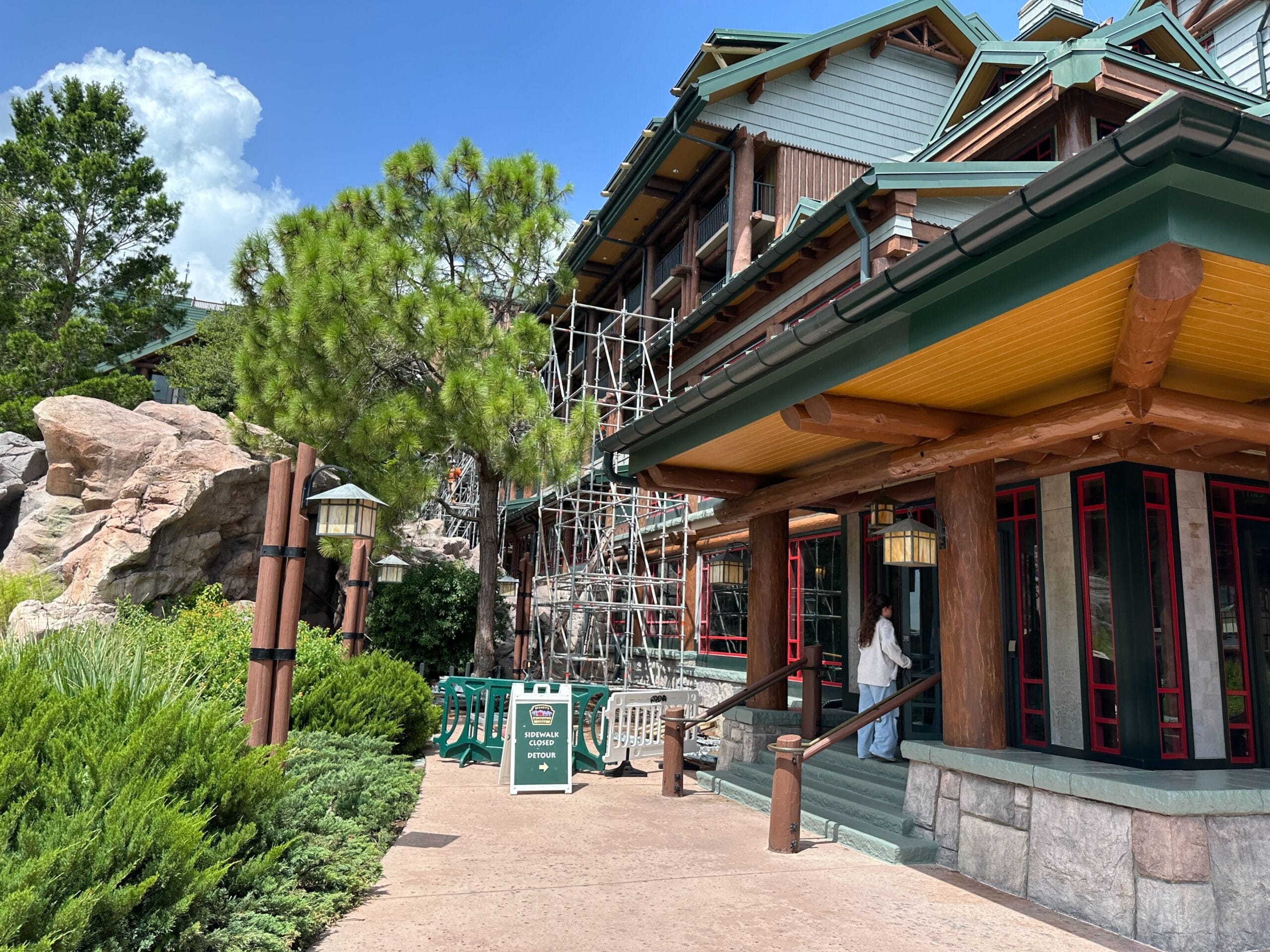 Scaffolding on the side of a rustic lodge building; a sign indicates a construction area.
