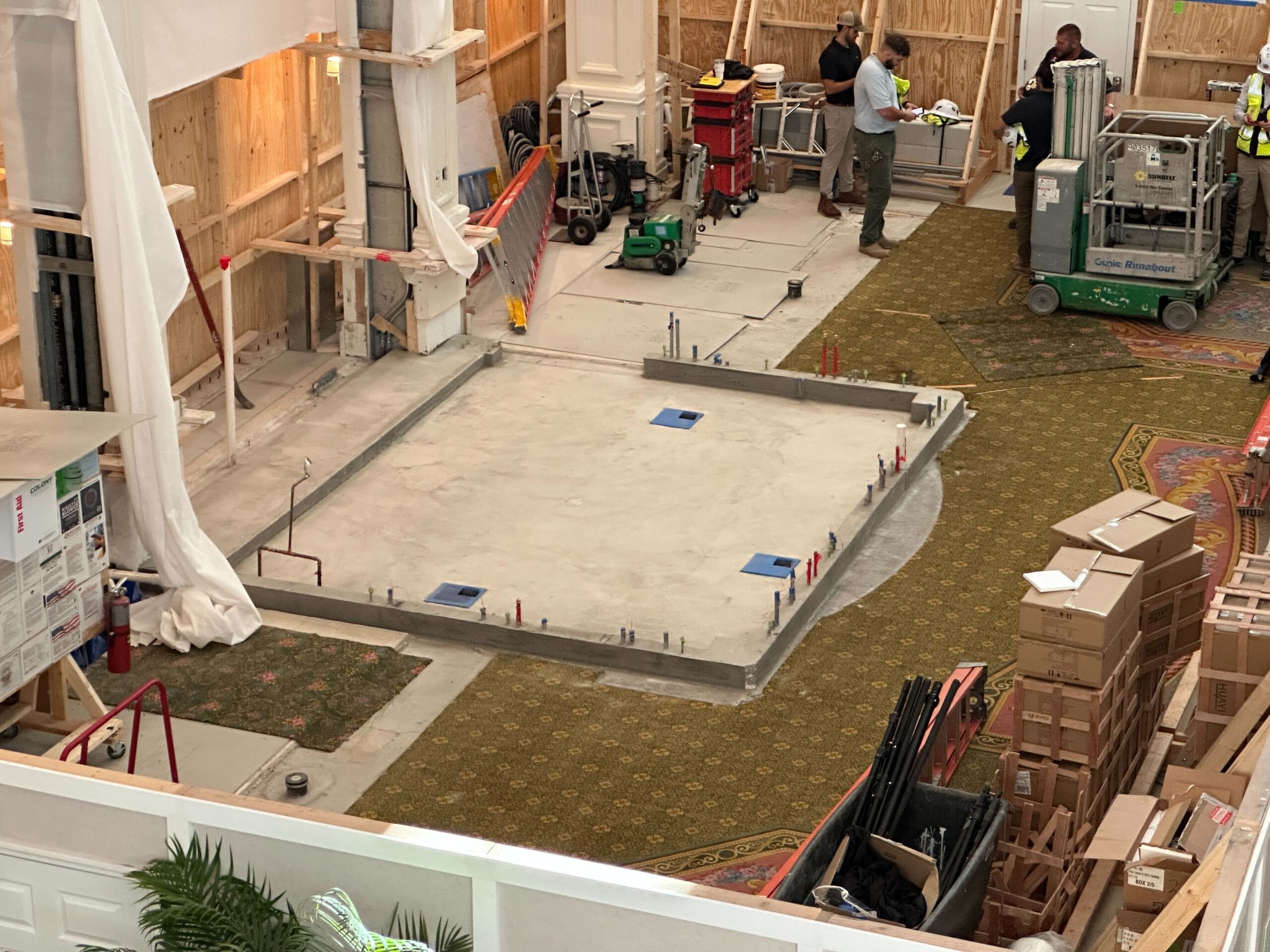 A construction area with tools, boxes, and workers inside a building with unfinished walls and exposed framing.