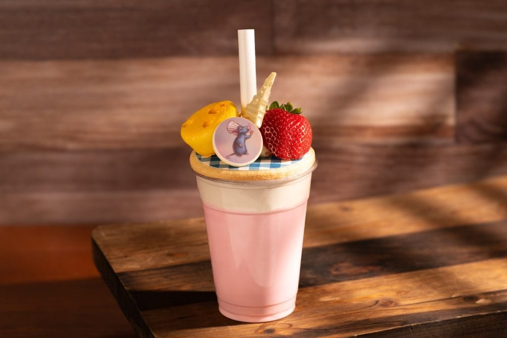 A pink milkshake from the 2025 menus, topped with a strawberry, cheese-shaped candy, and a cartoon mouse decoration.