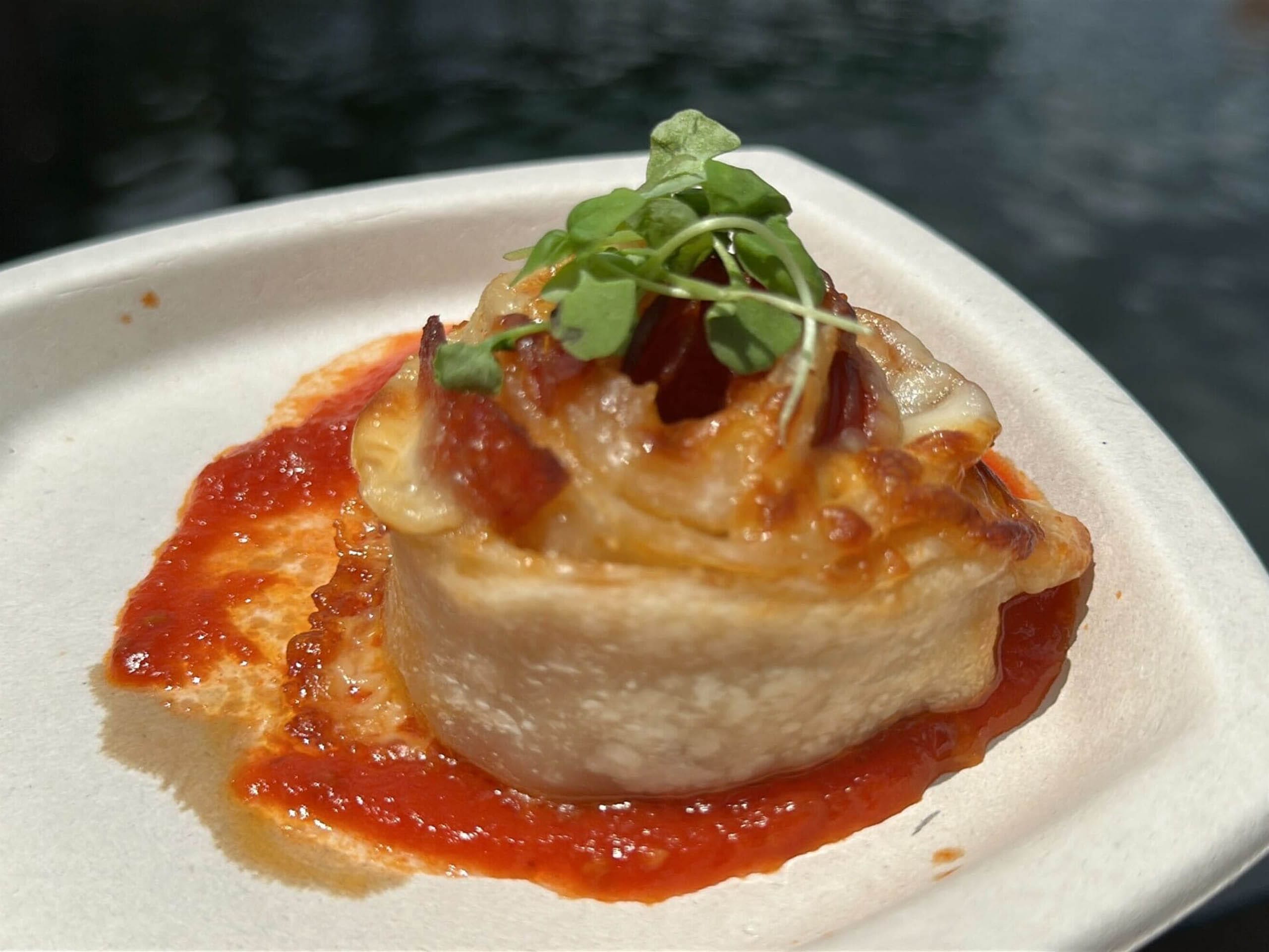 A baked roll topped with microgreens sits on a plate with red tomato sauce at EPCOT’s Food and Wine Festival.
