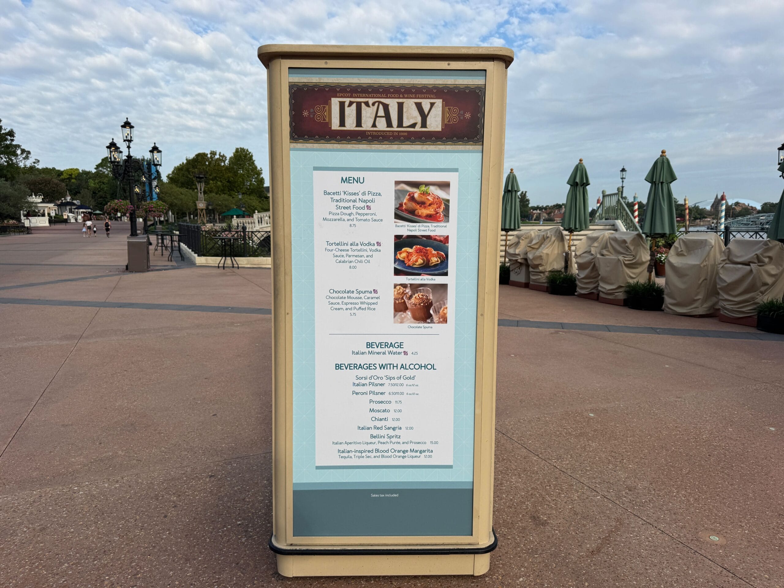 Outdoor Food & Wine menu sign at the Italy pavilion, with seating and umbrellas in the background.