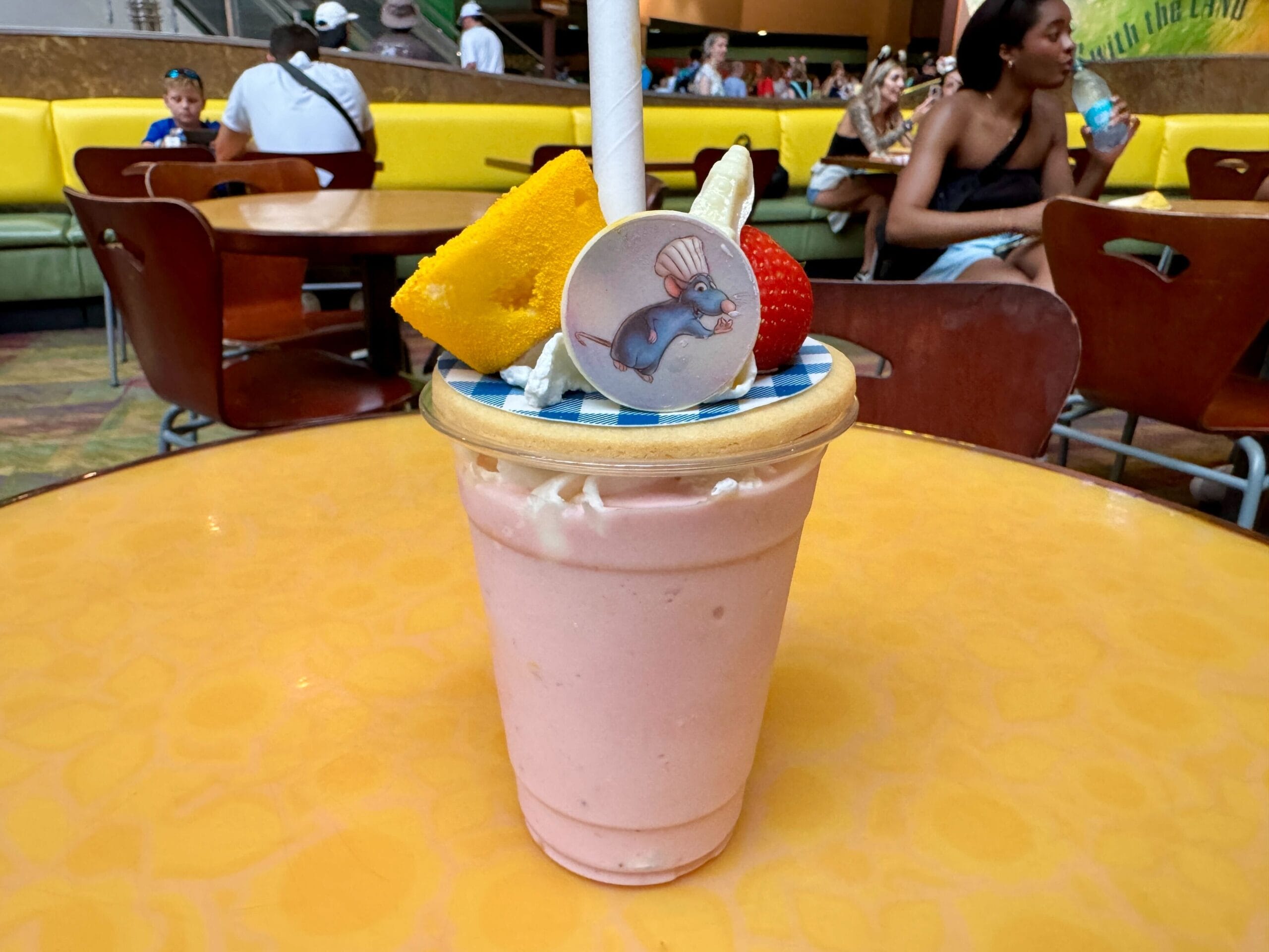 A strawberry milkshake topped with cake and a cartoon chef mouse, perfect for Food & Wine lovers at a restaurant.