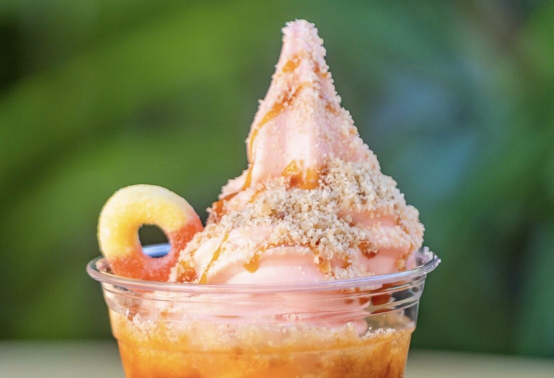 Peach Sundae featuring peach-colored soft serve, crumbly bits, caramel drizzle, and a peach ring candy—like a Disneyland treat!