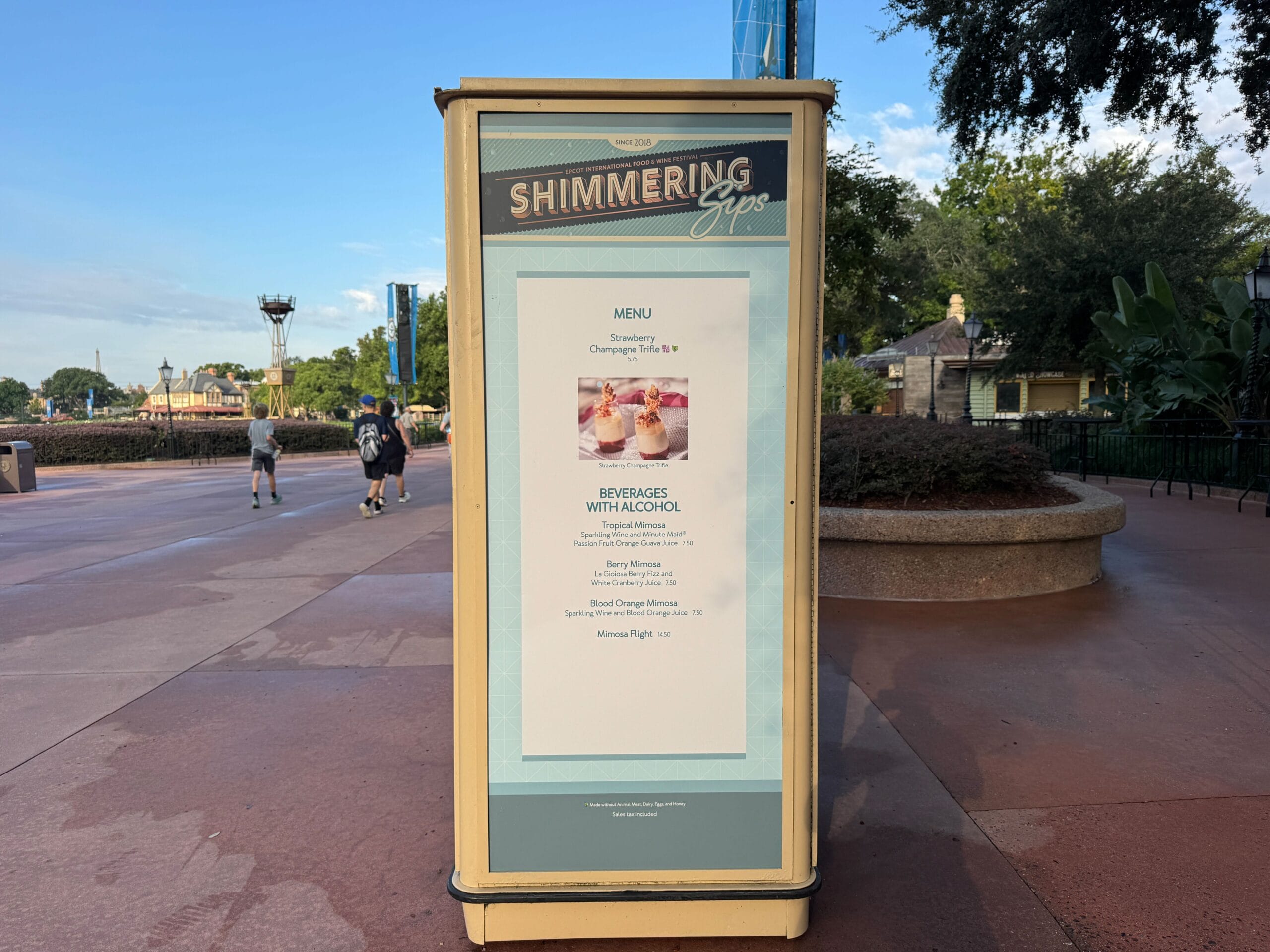 Outdoor Food & Wine menu sign for "Shimmering Sips" listing alcoholic beverages, with people walking in the background.