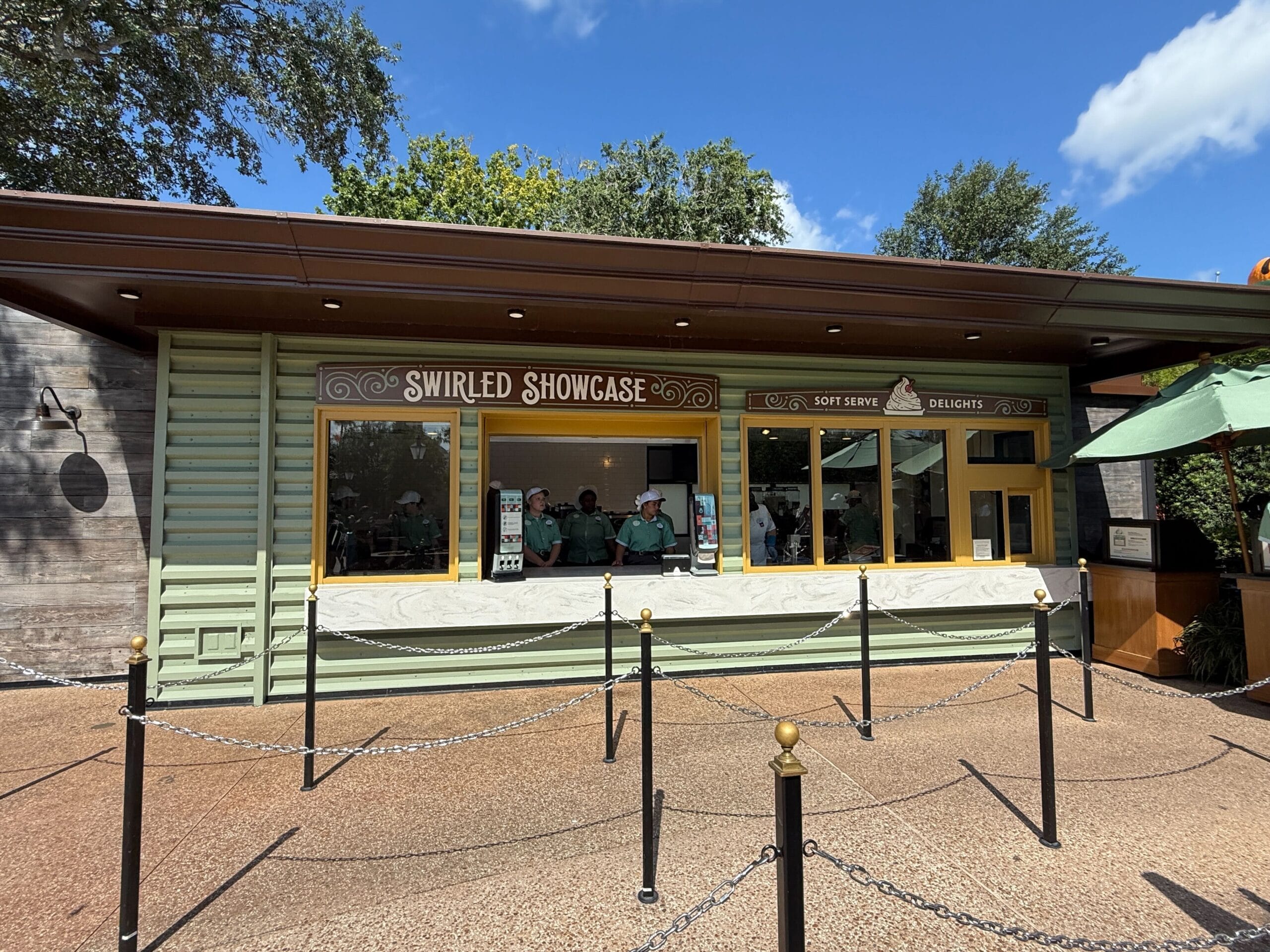 Swirled Showcase stand with Food & Wine signs, people inside, sunny day, and rope queue in front.