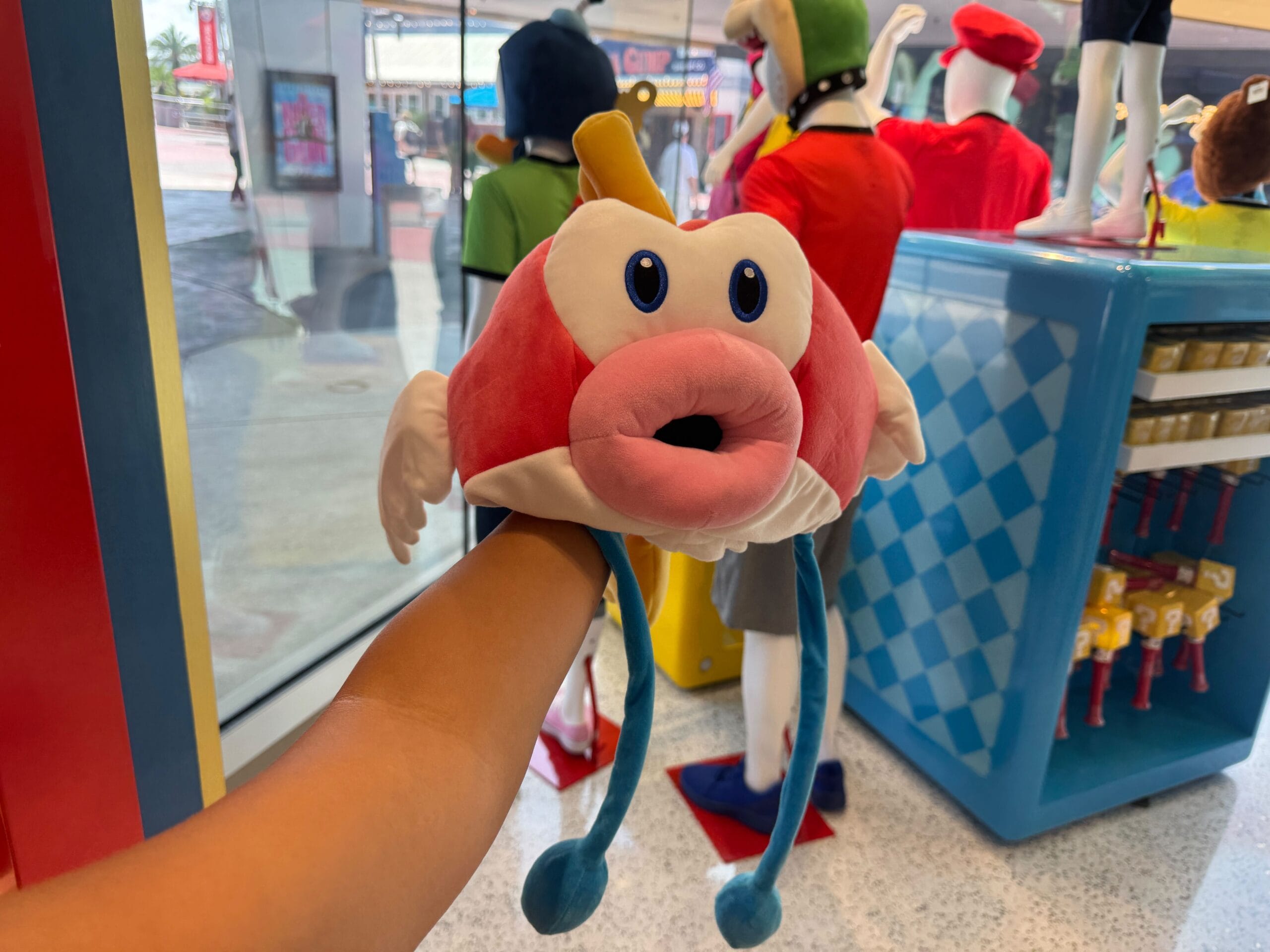 A person holds a new Cheep Cheep Hat with big eyes and blue tassles inside a colorful Universal Studios store.