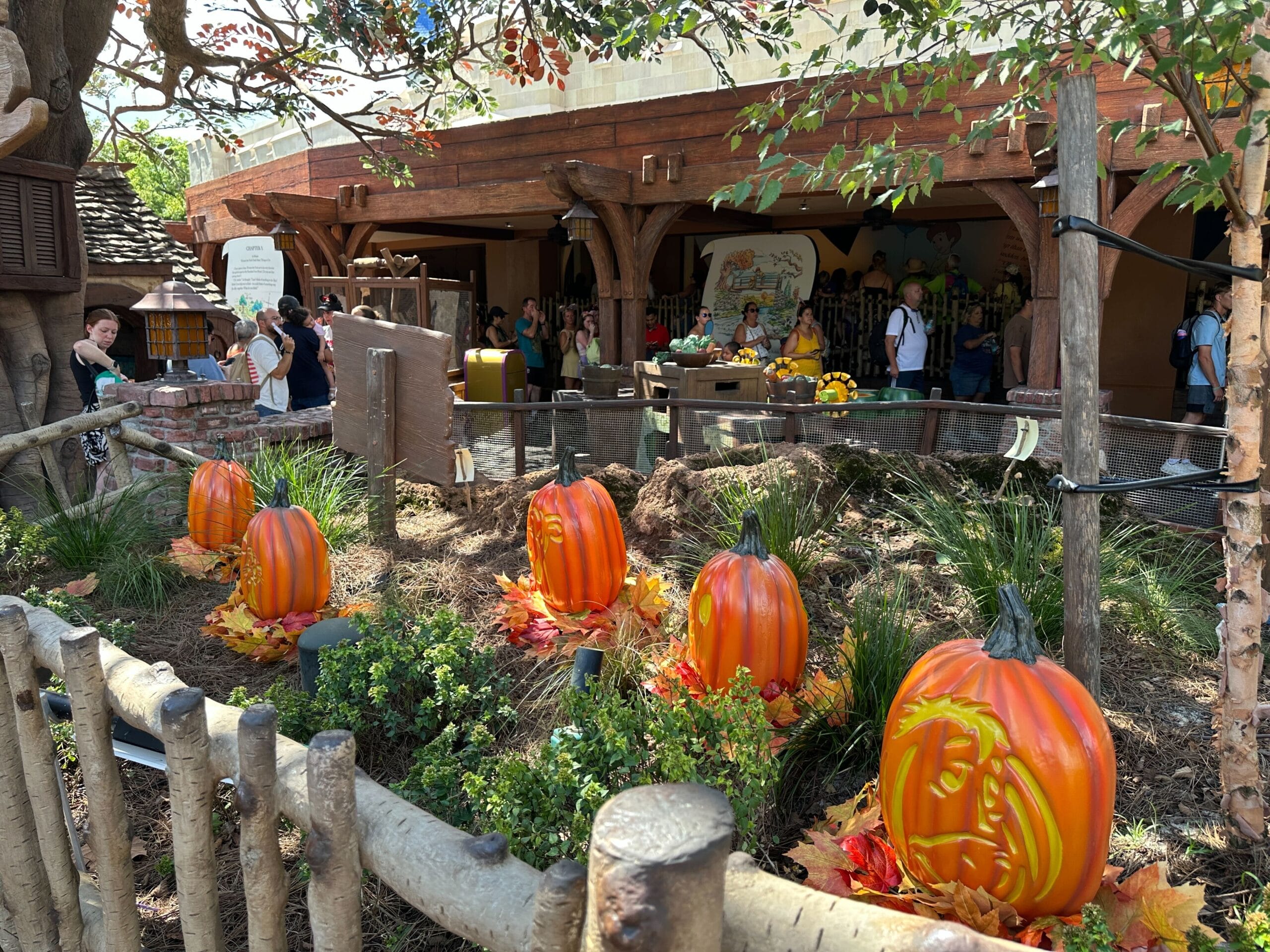 Four large orange pumpkins with autumn leaves create festive Halloween Decorations in a fenced garden at a busy outdoor park.