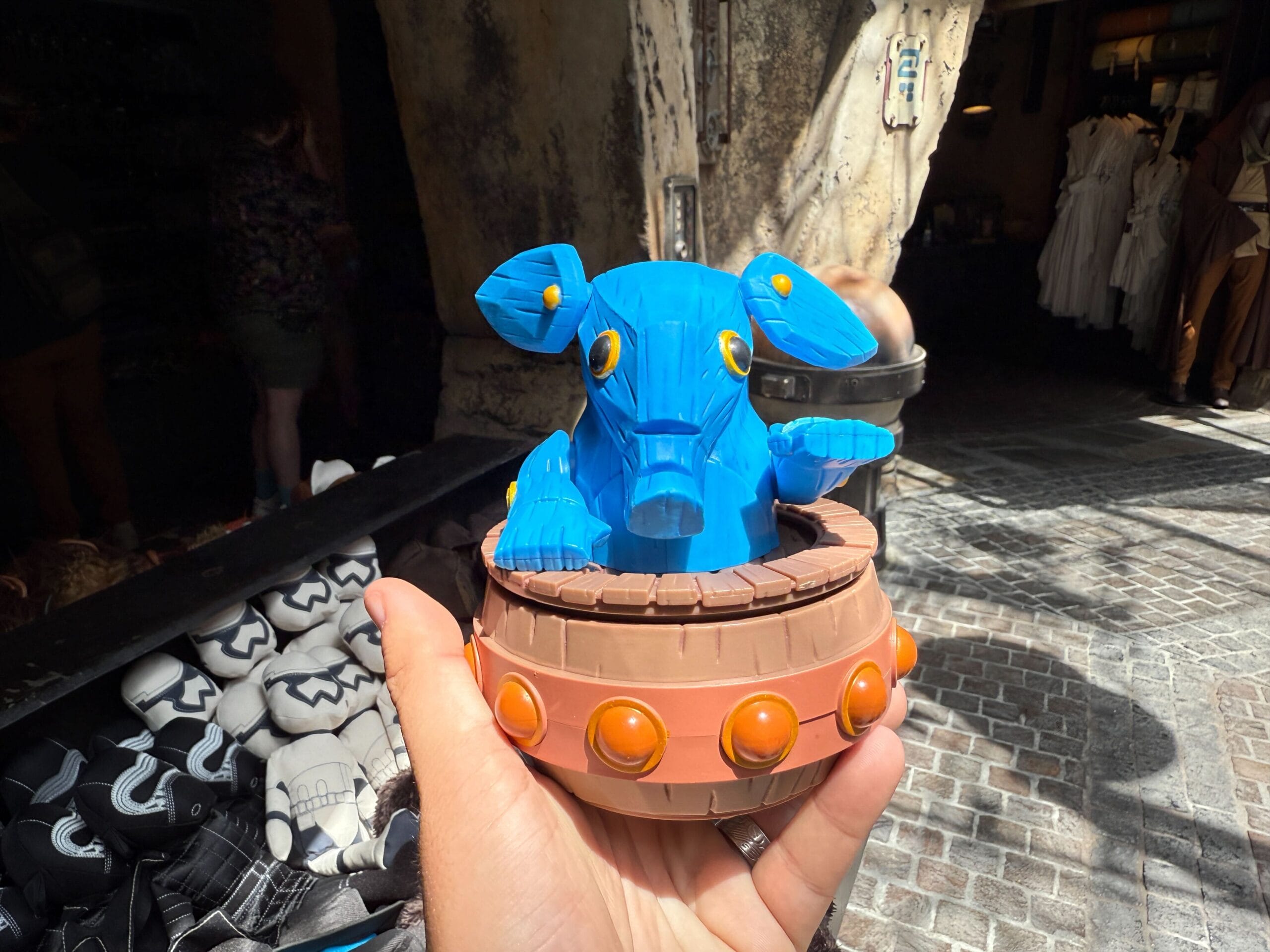 A hand holds a Max Rebo figure with yellow eyes in a brown base at the Star Wars Galaxy's Edge market.