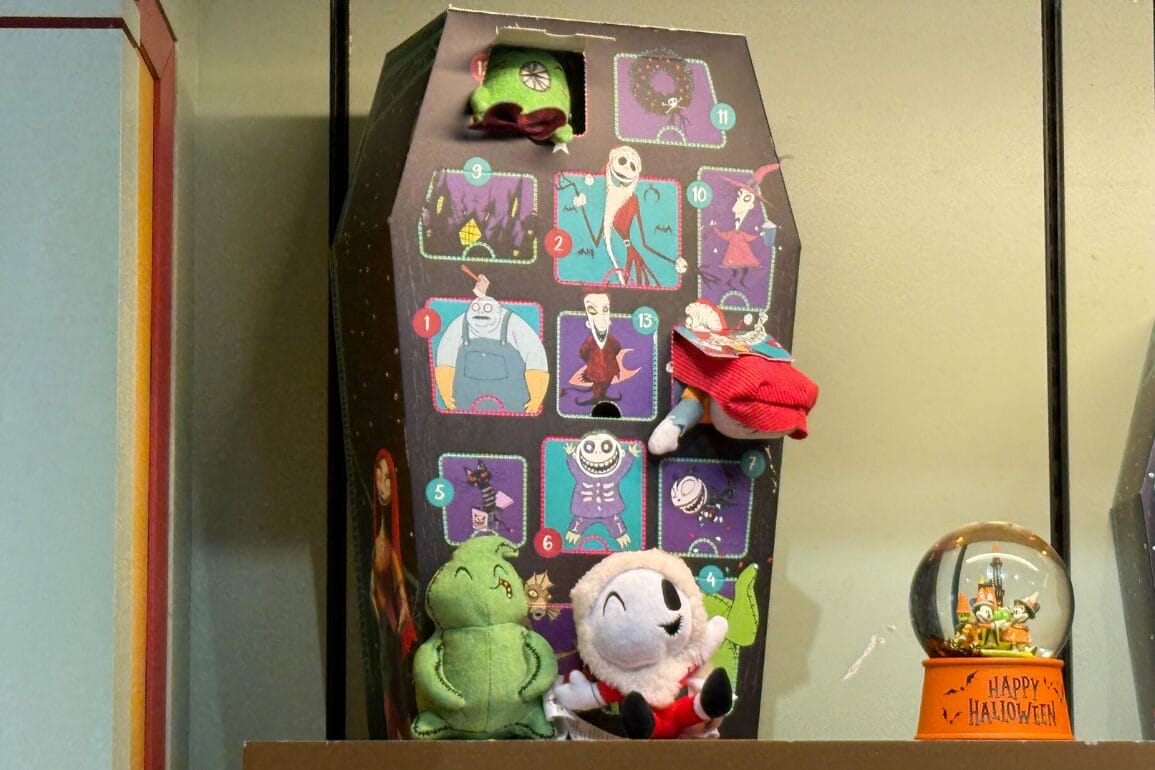 Plush toys and a Nightmare Before Christmas Advent Calendar sit on a shelf next to a Halloween snow globe.