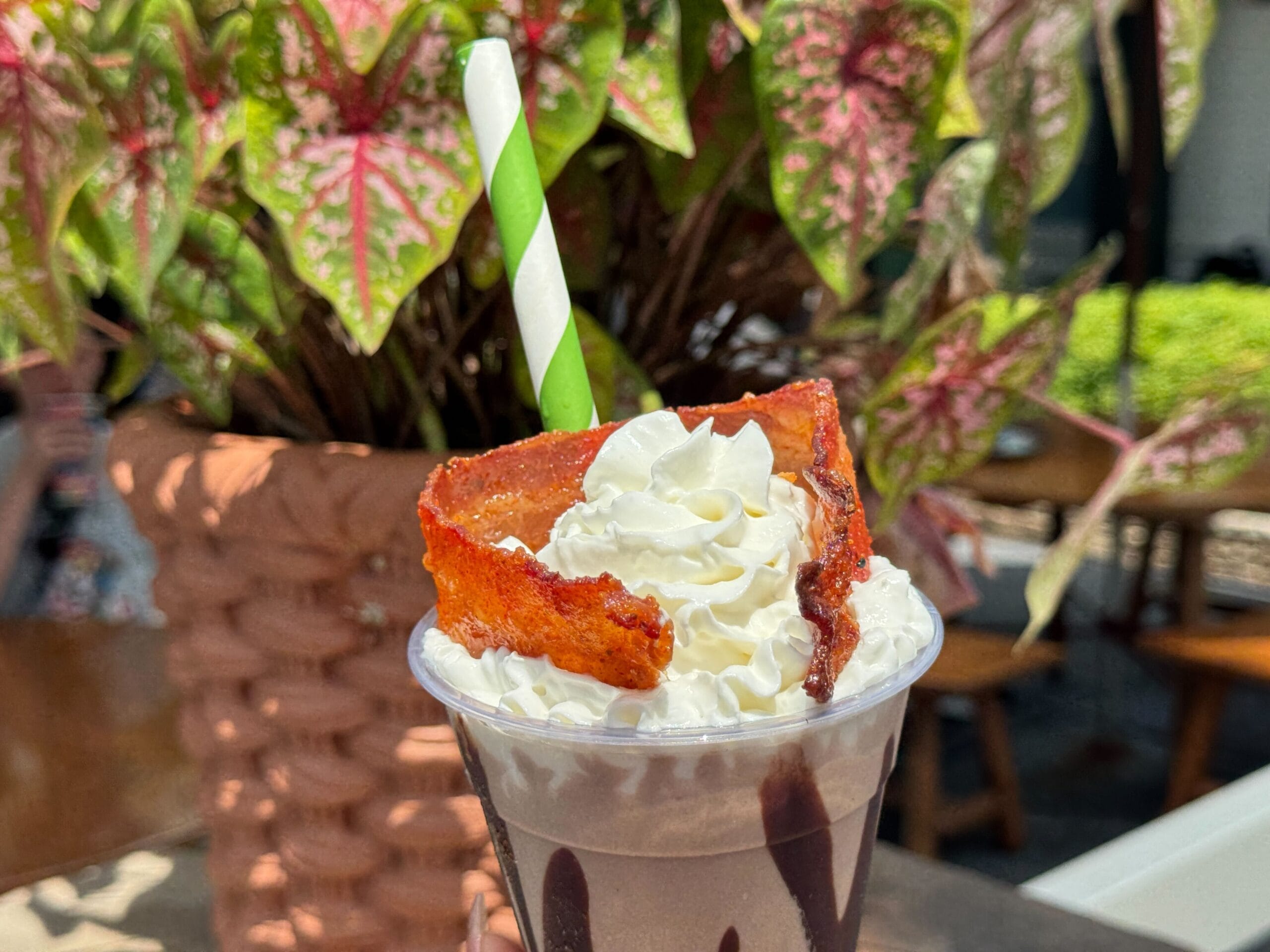 Chocolate Bourbon Milk Shake with whipped cream and bacon, topped with a green-striped straw, served outdoors.