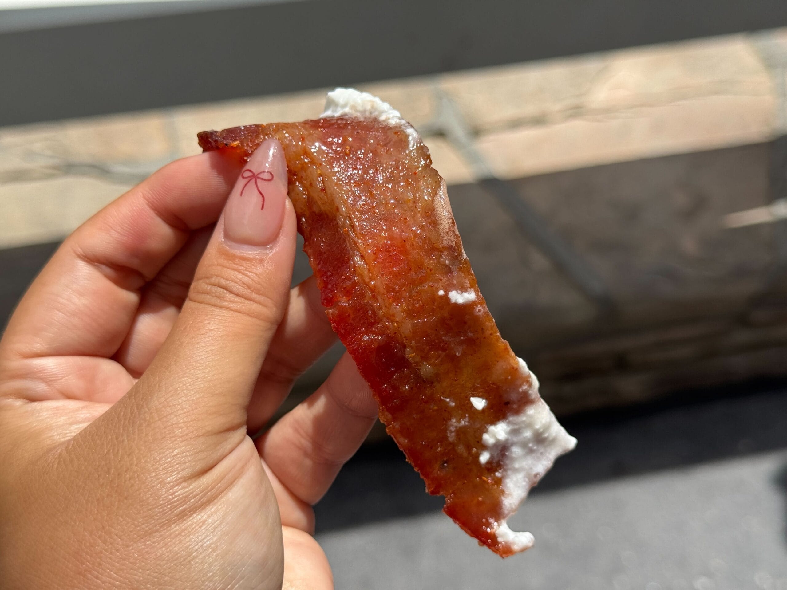 A hand holding a strip of glazed bacon with a white creamy topping at Disney's Hollywood Studios.
