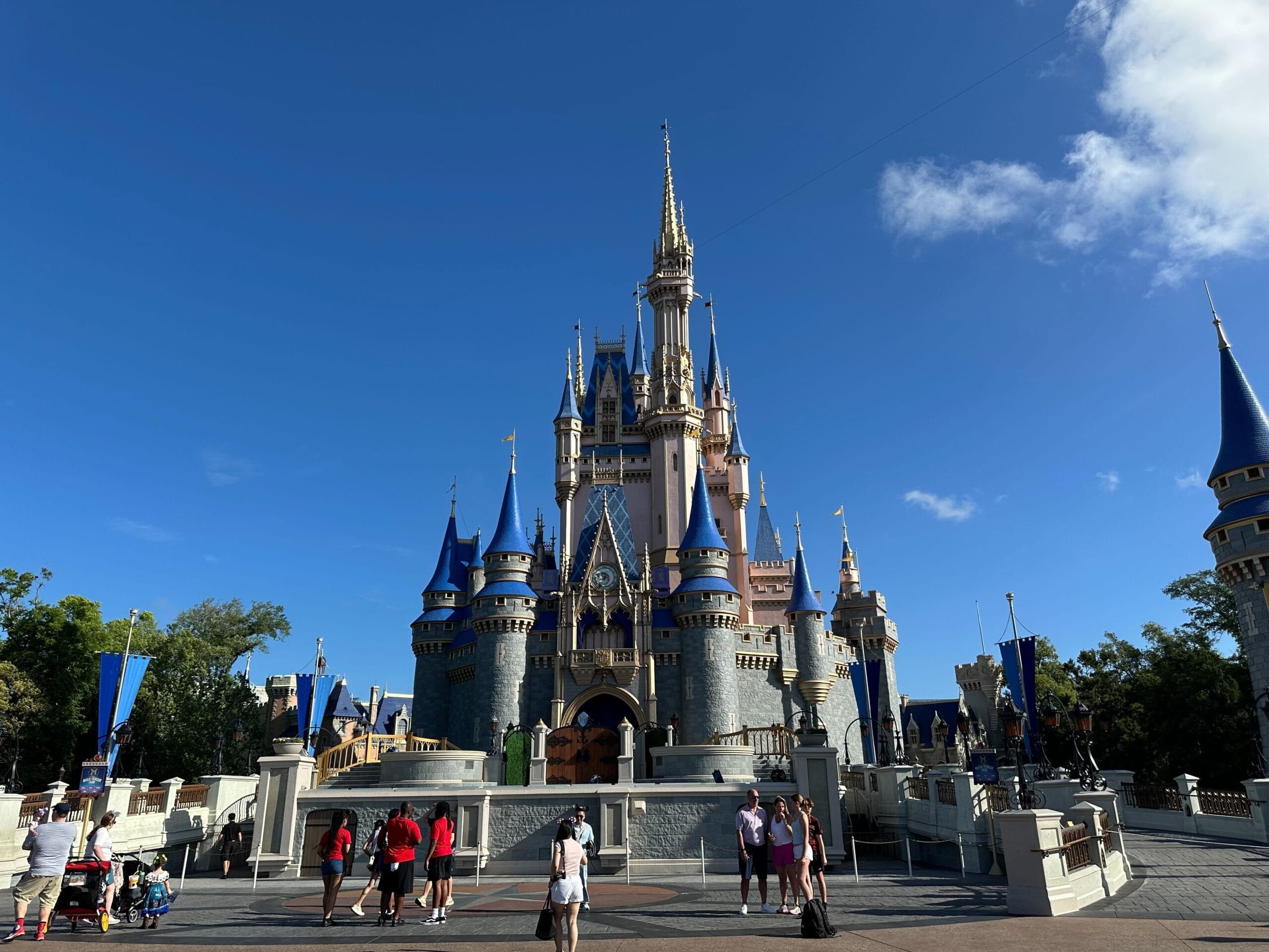 People stand in front of Cinderella Castle at Walt Disney World on a record sunny day with a clear blue sky.