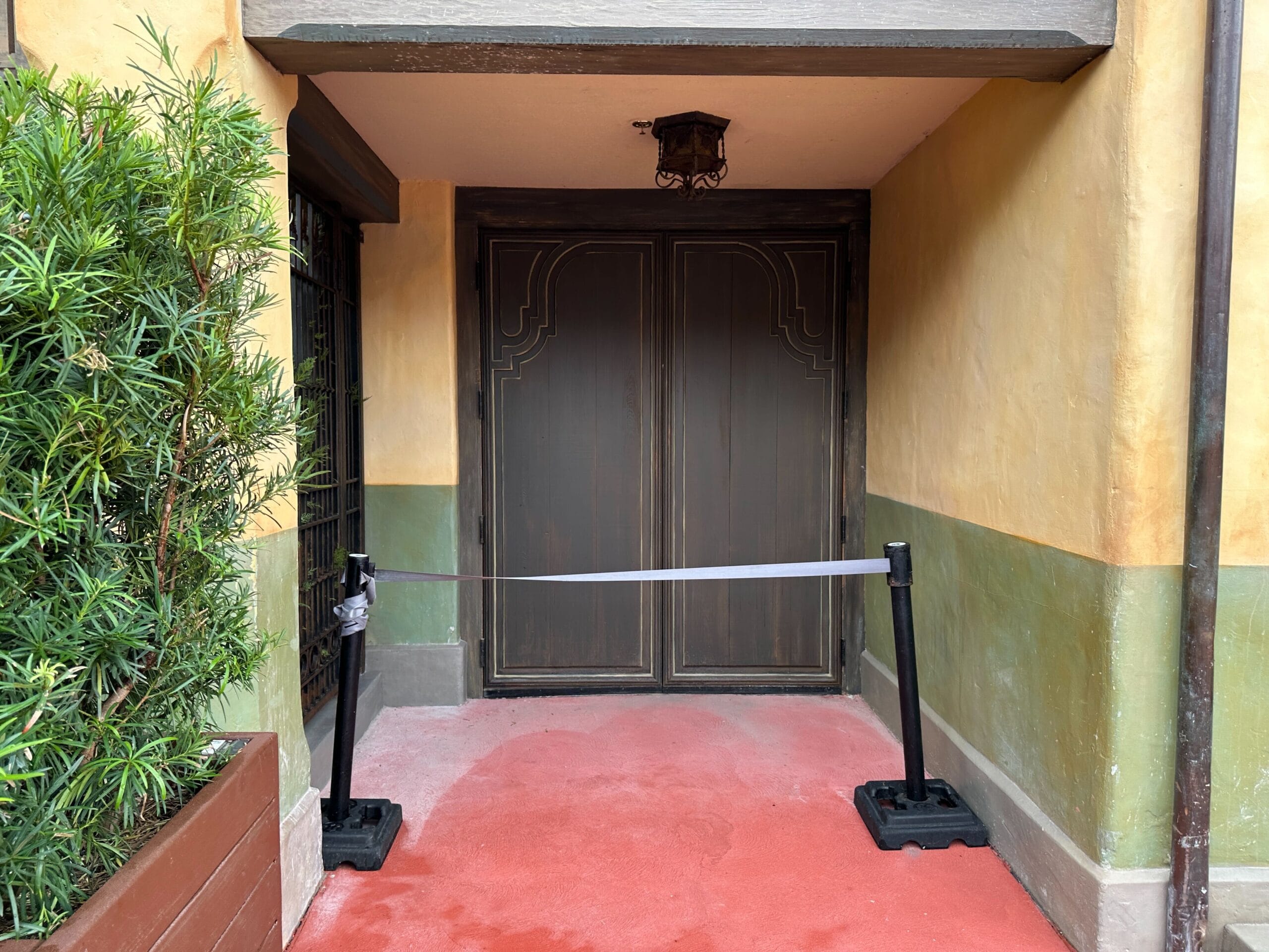 Brown double doors blocked by a ribbon barrier near painted yellow-green Construction Walls at Magic Kingdom.