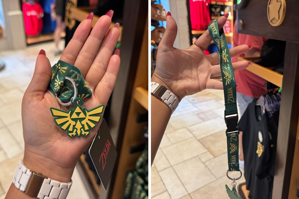 A hand holds a green Legend of Zelda lanyard keychain with a yellow Hylian Crest.