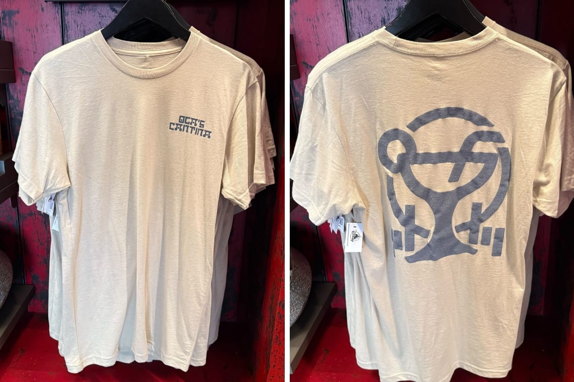Front and back of beige-colored Oga's Cantina t-shirt hanging in A new Oga's Cantina shirt has landed alongside last month's glassware drop at Disneyland Resort.