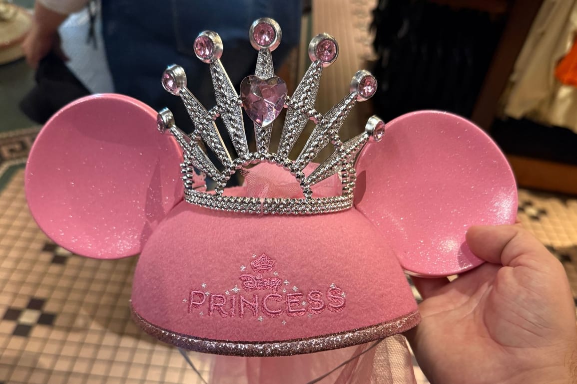 A hand holds a Pink Princess Ear Hat with sparkling tiara at Disneyland Resort.