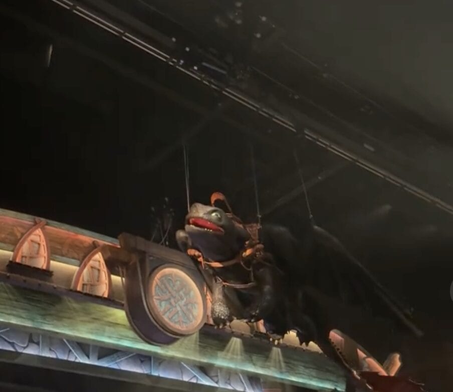 A large Toothless dragon puppet hangs above a Viking-themed stage show set with shields at Epic Universe.