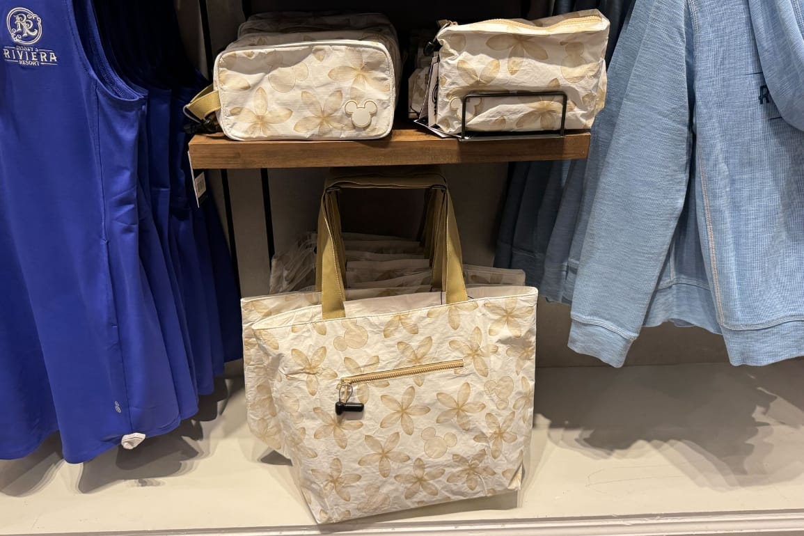 Cream-colored Aloha Collection Bags with a light floral pattern displayed on a shelf next to blue clothing in a store.
