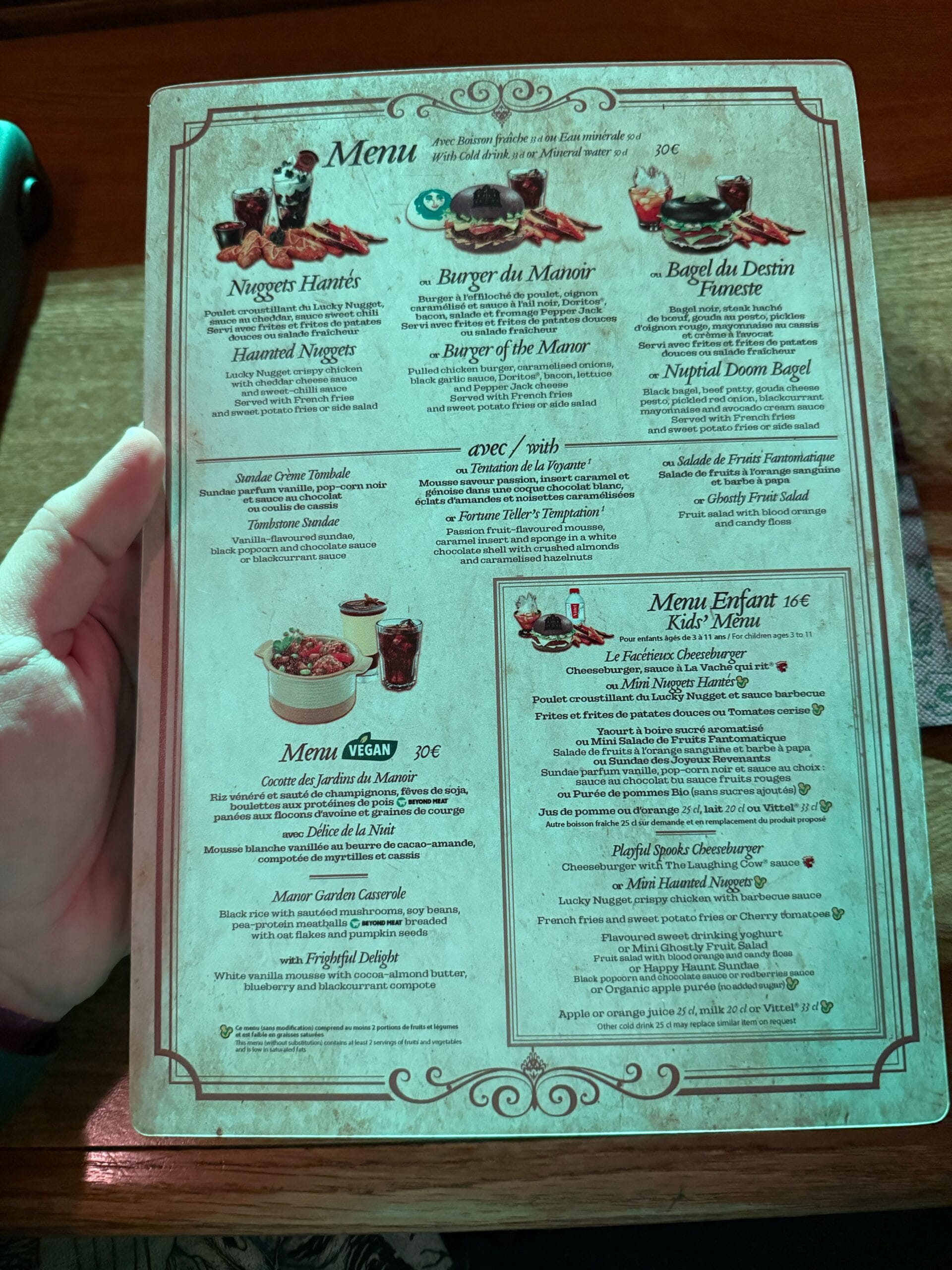 A hand holds a vintage-style Unlucky Nugget Saloon menu with French and English food options and decorative borders.