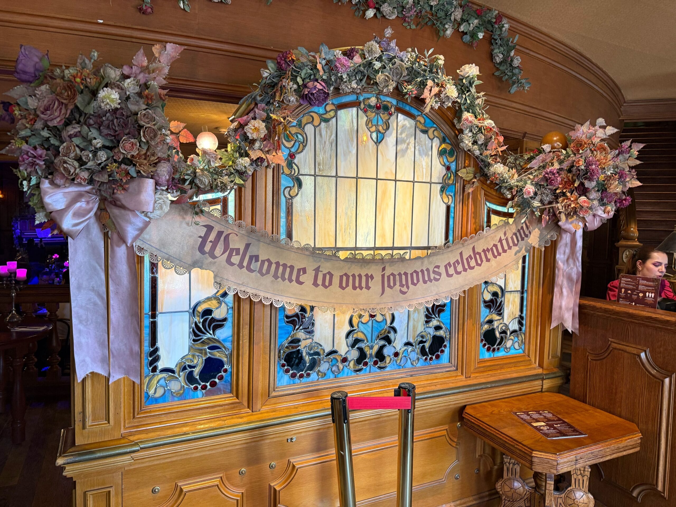 Floral arch and banner greet you on a stained glass wooden partition at Unlucky Nugget Saloon in Disneyland Paris.